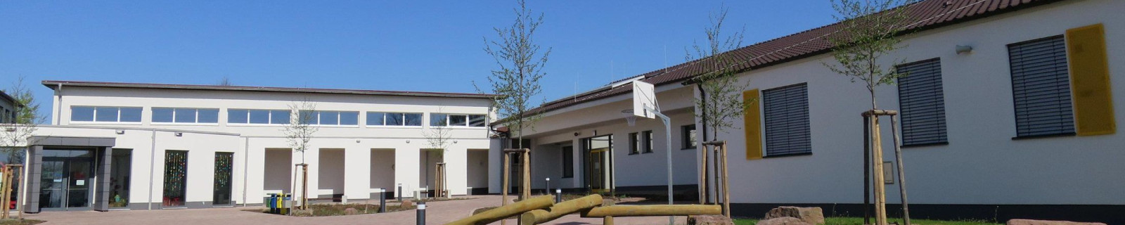 Außenansicht eines modernen Schulgebäudes mit gepflastertem Hof und blauen Himmel.