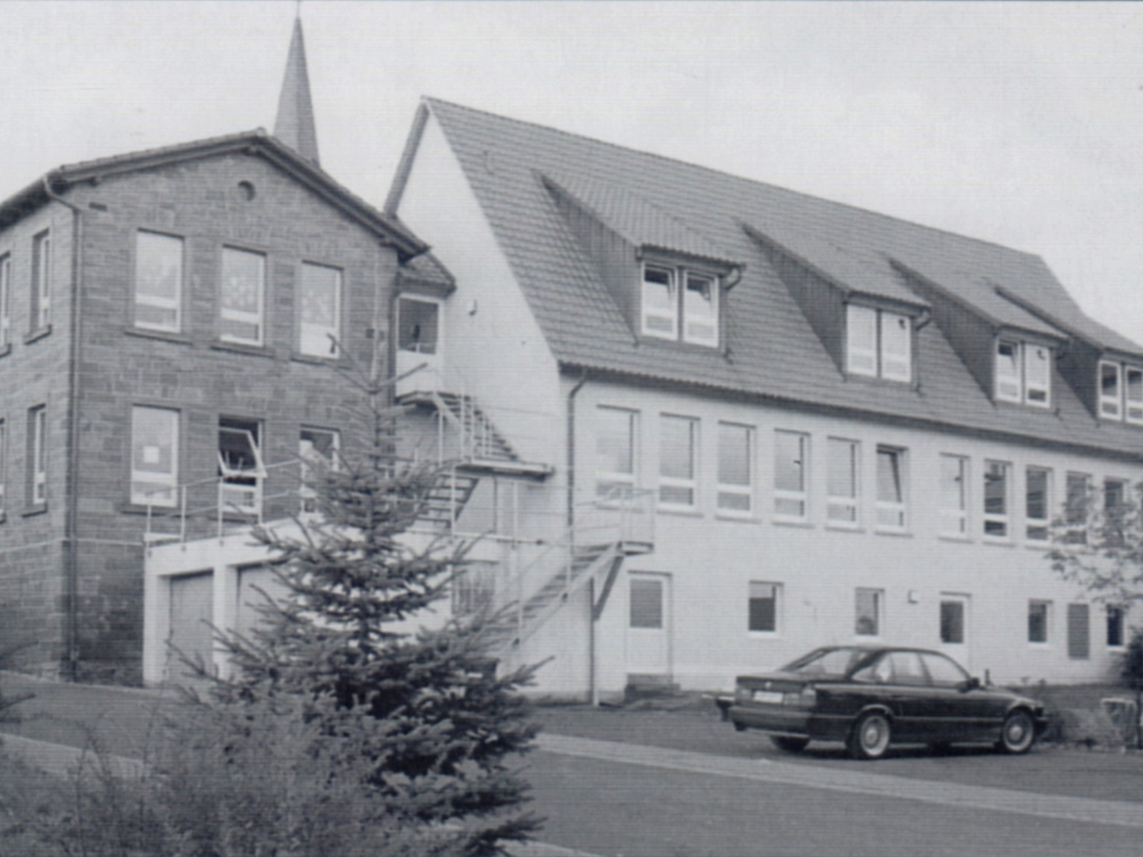 Historisches Gebäude mit Treppe außen, Satteldach und geparktem Auto vorne.
