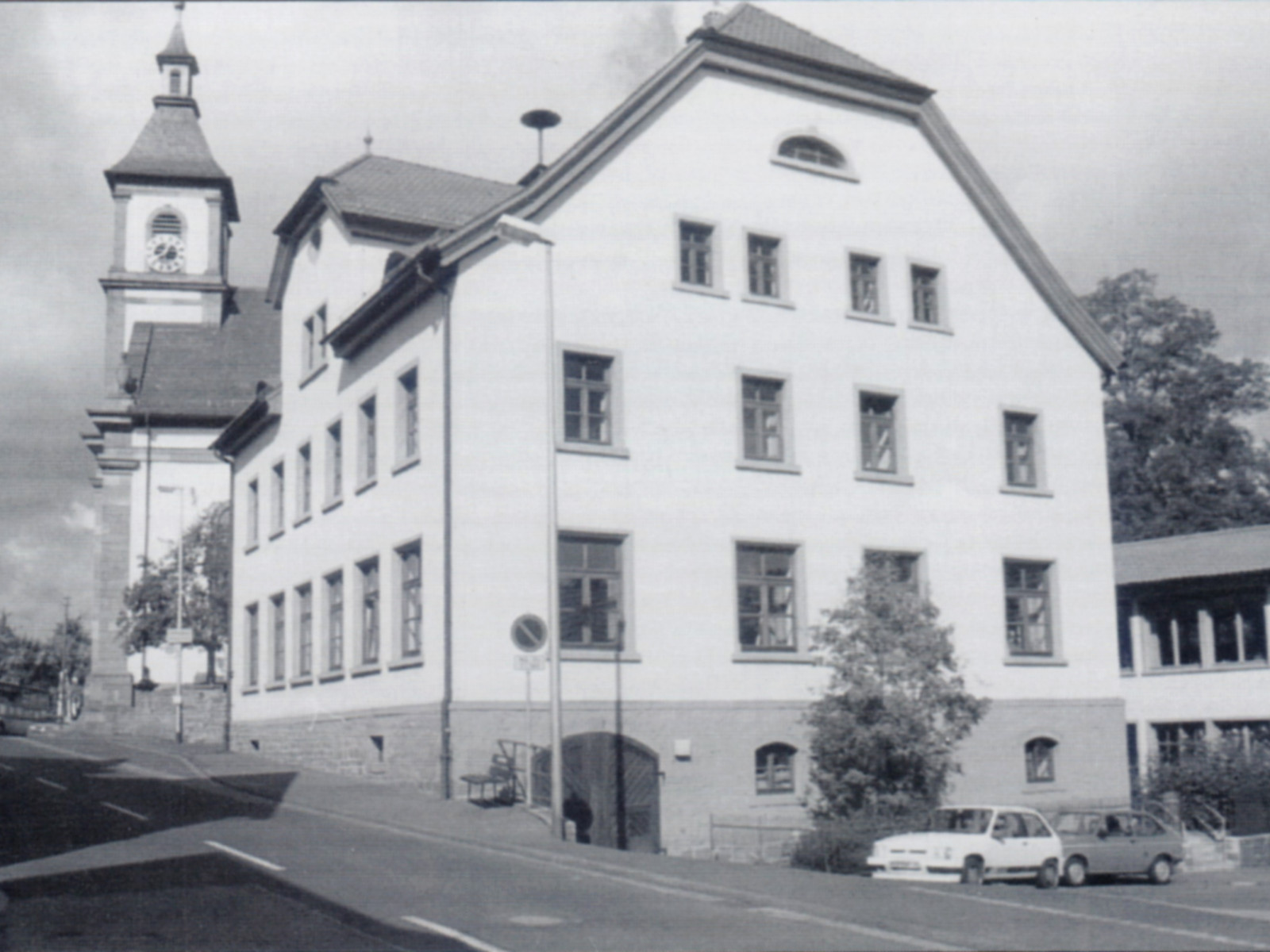 Ein großes, altes Gebäude mit einem Kirchturm im Hintergrund und einem Auto im Vordergrund.