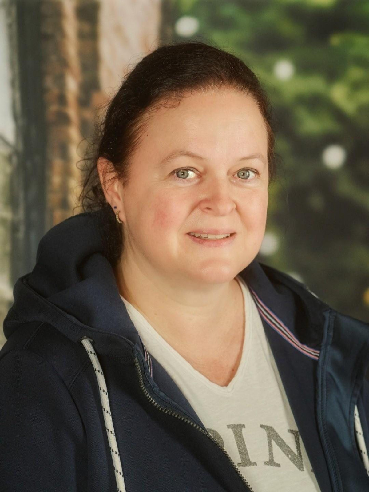 Frau mit dunkelbraunen Haaren in Freizeitkleidung vor unscharfem Hintergrund.