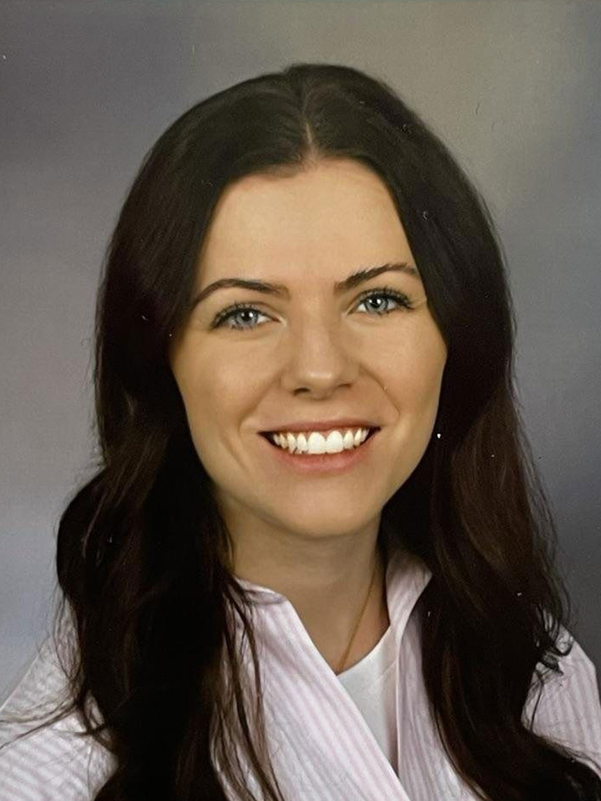 Porträtfoto einer lächelnden Frau mit langen dunklen Haaren in hellem Oberteil.
