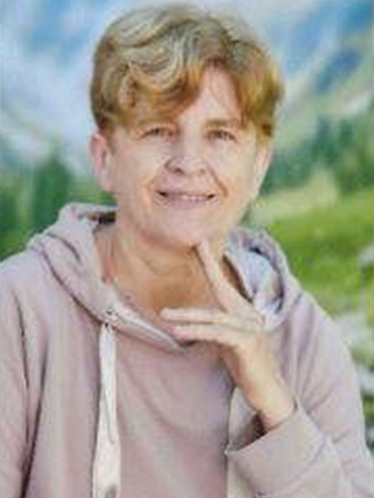 Frau in beiger Kapuzenjacke vor einer unscharfen Naturkulisse.