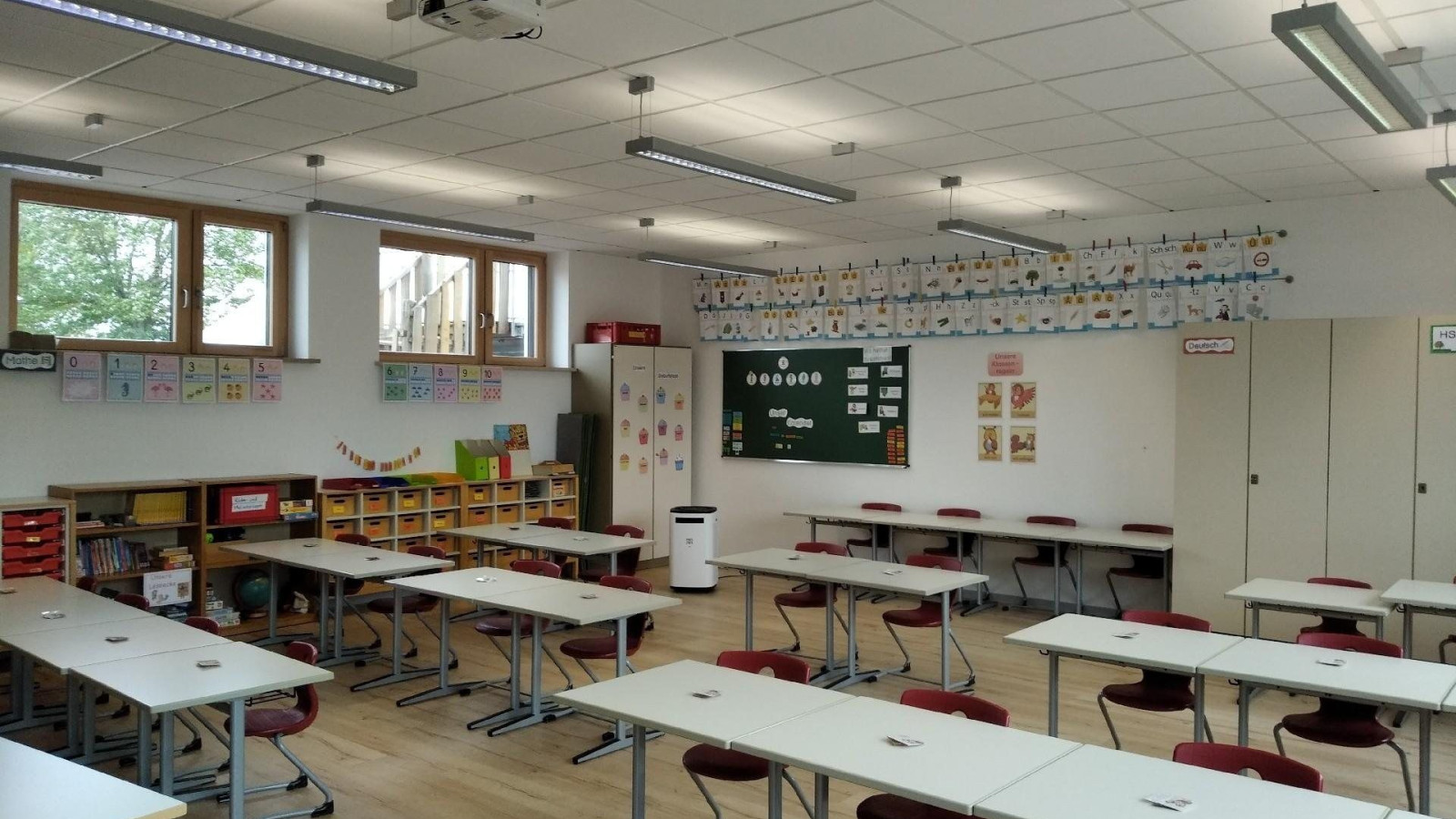 Ein modernes Klassenzimmer mit Schultischen, Stühlen und einer Tafel an der Wand.