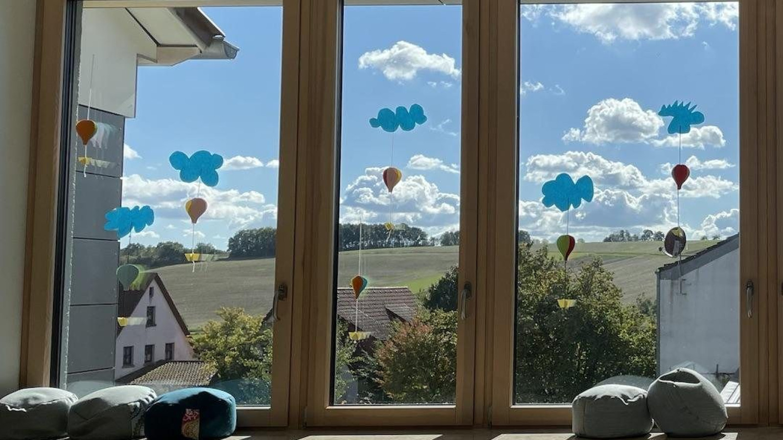 Großes Fenster mit Dekorationen von Wolken und Heißluftballons, dahinter Landschaft und Himmel.