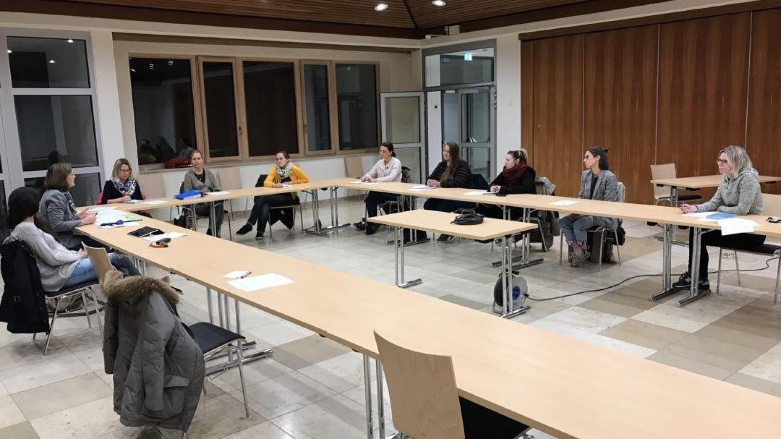 Personen sitzen in einem modernen Konferenzraum an einem U-förmigen Tisch und diskutieren.