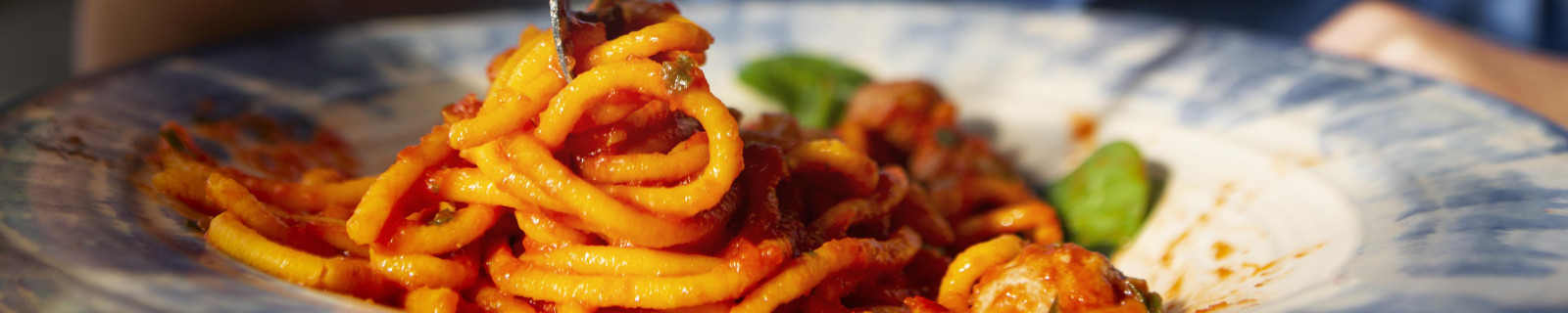 Ein Junge in blauem Hemd isst Spaghetti mit Tomatensauce und lächelt in die Kamera.