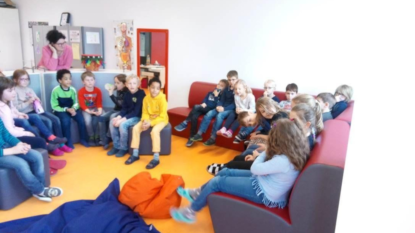 Kindergruppe auf Sofas in einem Klassenraum, aufmerksam zuhörend.