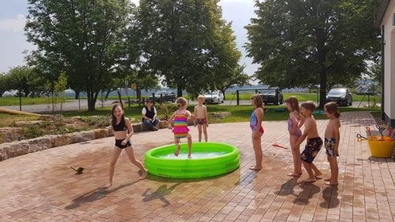 Kinder in Badebekleidung spielen um ein kleines aufblasbares Planschbecken im Freien.