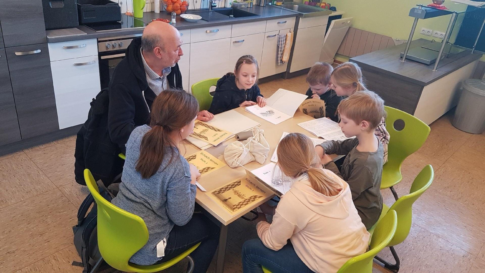 Kinder und ein Lehrer sitzen an einem Tisch, blicken auf Unterlagen und arbeiten gemeinsam.