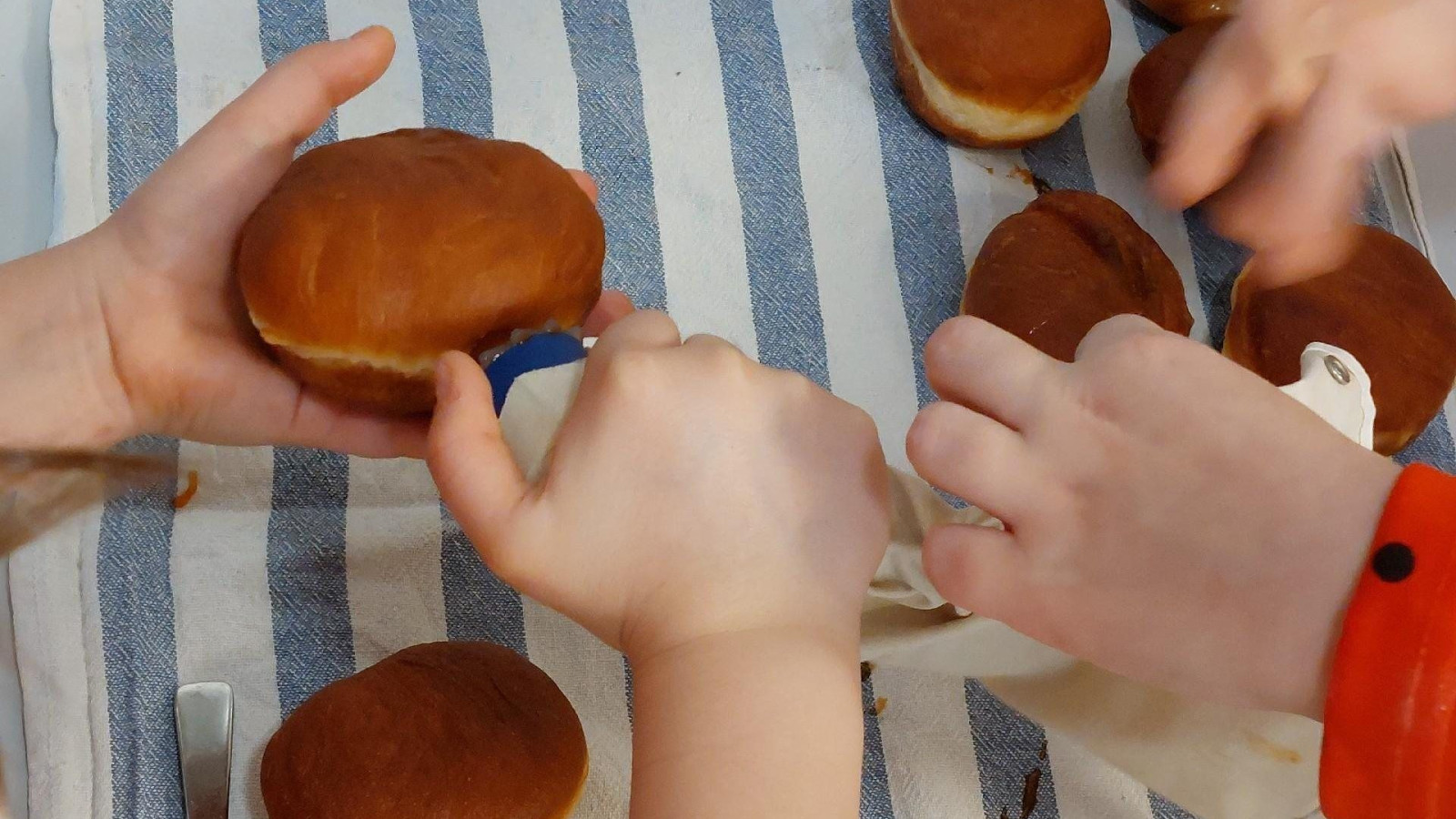 Kinder befüllen Berliner auf einem gestreiften Tuch mit Marmelade.