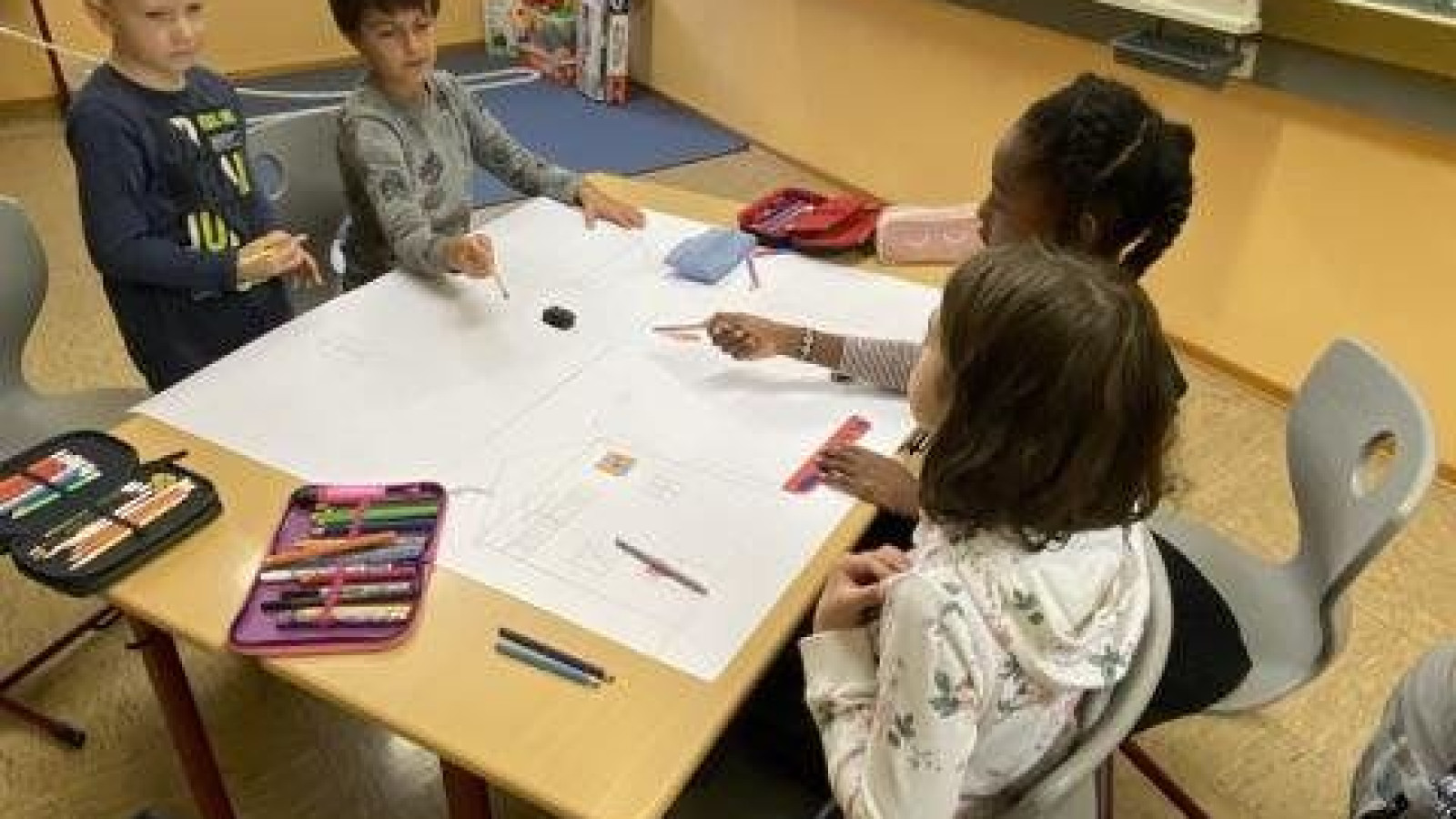 Gruppe von Kindern in einem Klassenzimmer, die gemeinsam an einem Tisch arbeiten.