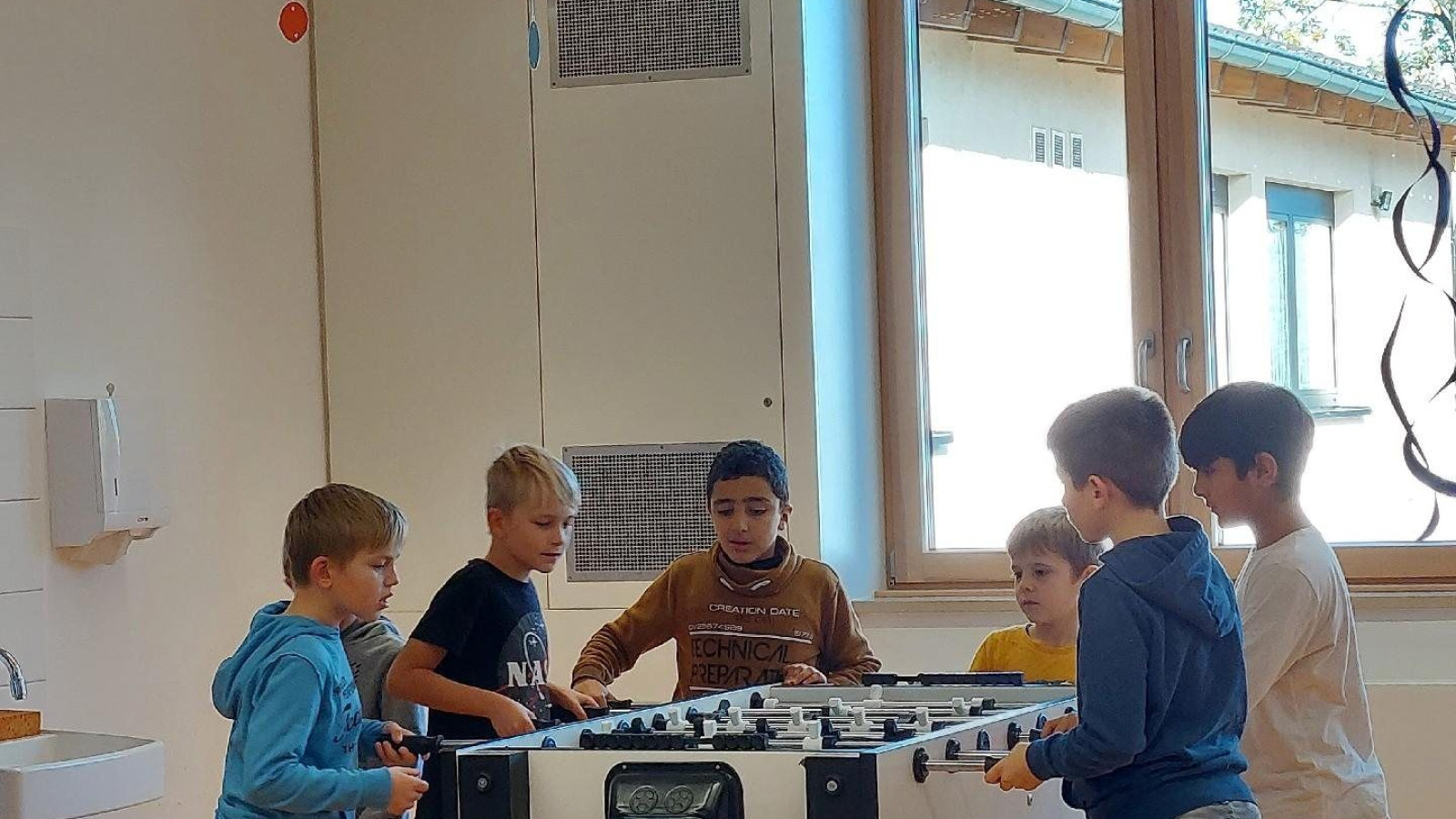Jungen versammeln sich um einen Tischfußballtisch in einem Klassenzimmer mit bunten Dekorationen.