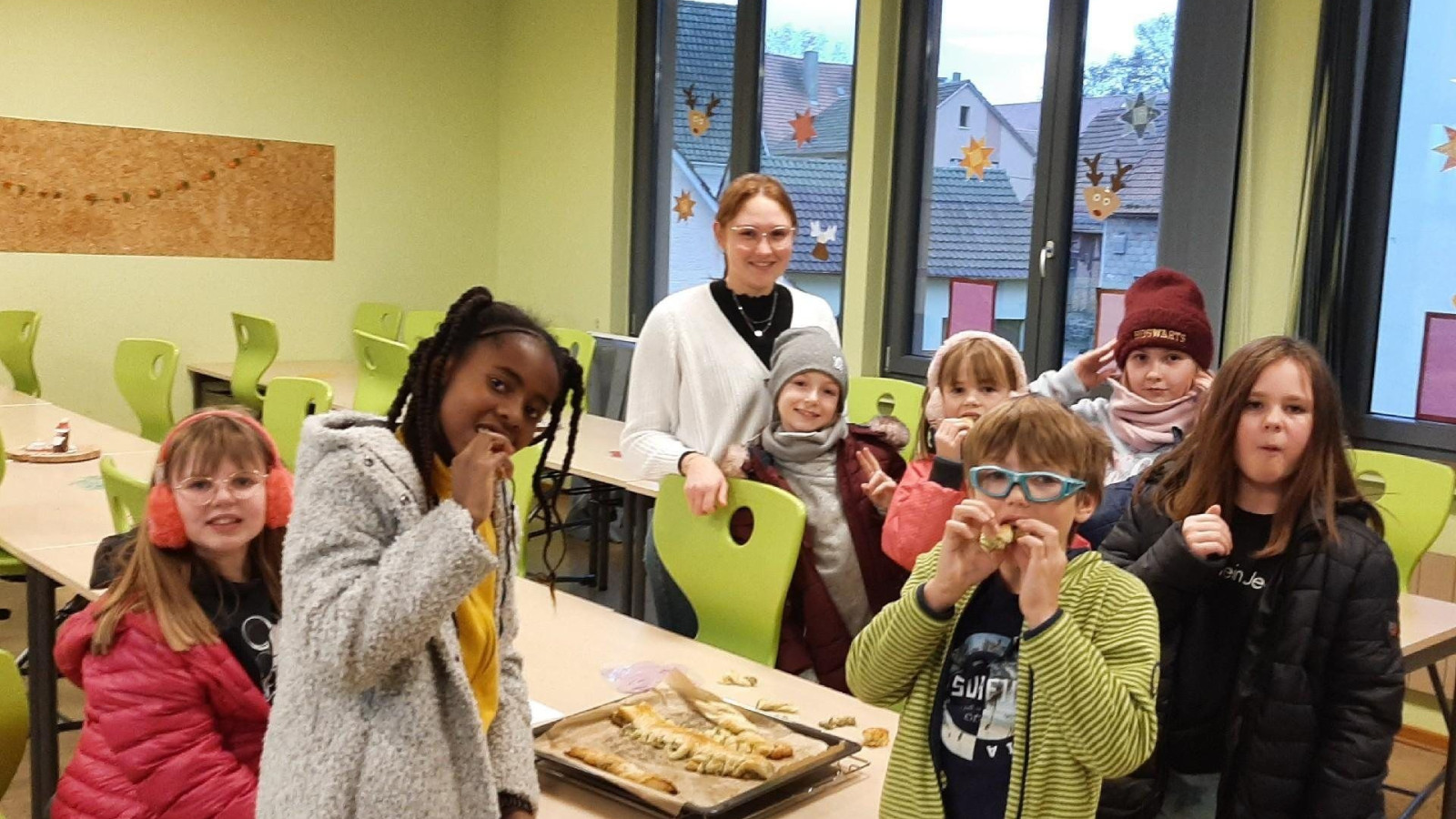 Gruppe von Kindern und Lehrerin in einer Schulküche. Kinder essen Gebackenes.