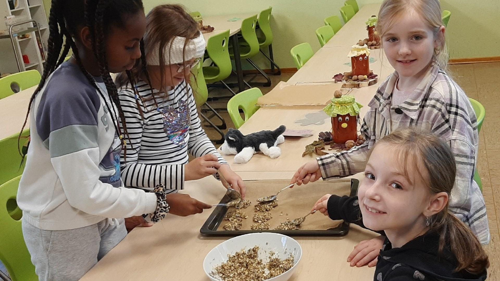 Vier Kinder stehen vor einem Tisch im Schulklassenzimmer, auf dem Bastelmaterialien liegen.