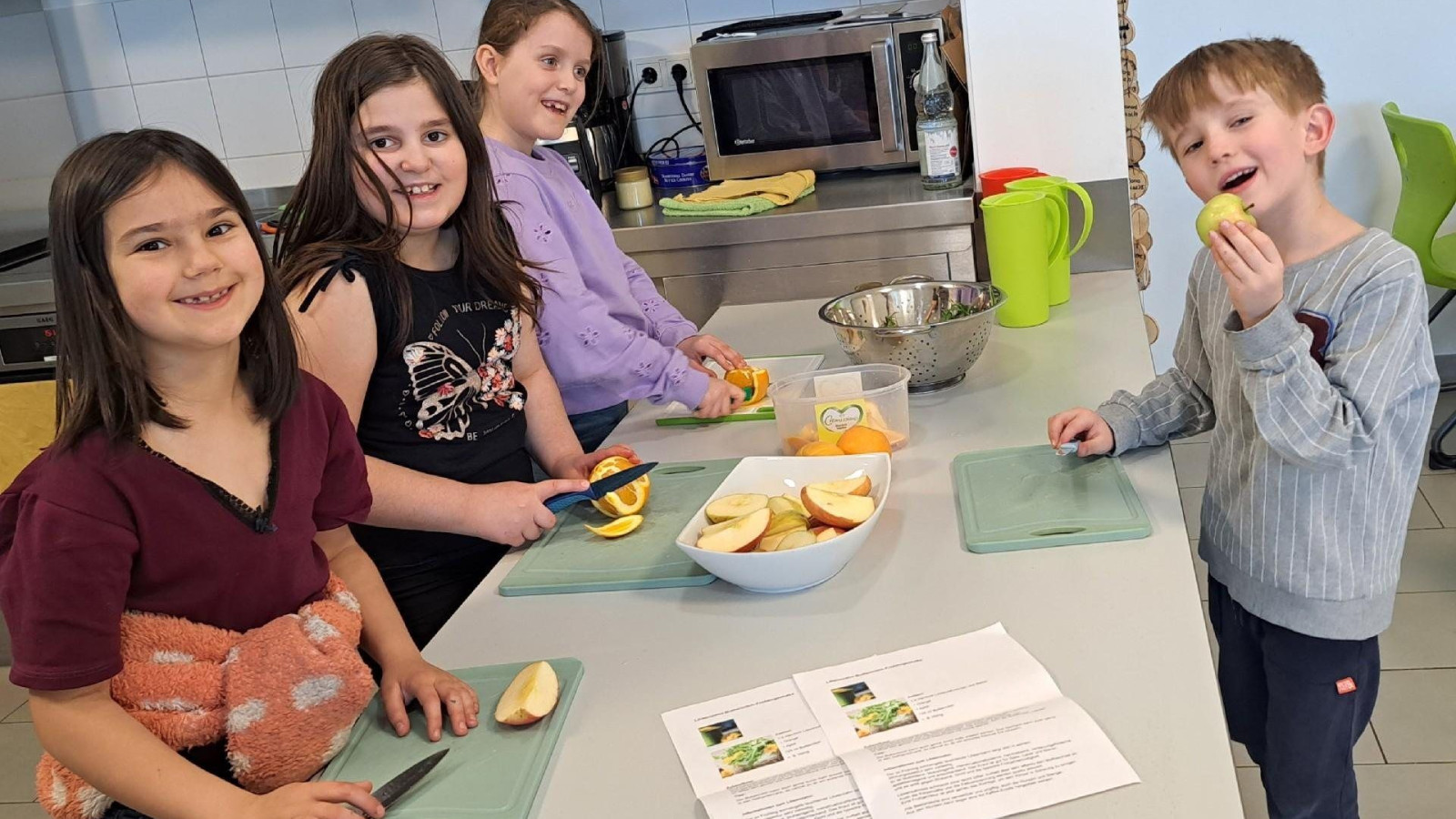 Vier Kinder stehen an einem Tisch in der Küche und schneiden Äpfel auf Schneidebrettern.