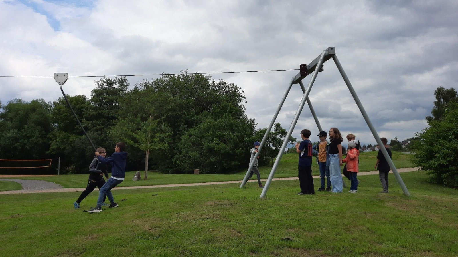 Kinder spielen auf einer Seilrutsche im Park, während andere zuschauen.
