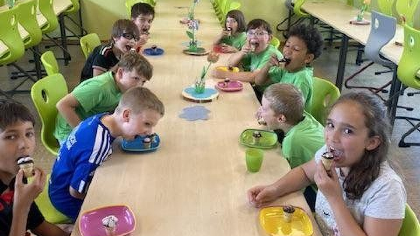 Kinder in einer Schulcafeteria, die an einem langen Tisch sitzen und essen.