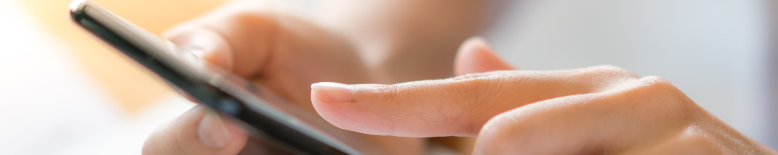 Nahaufnahme einer Hand, die ein Smartphone hält und darauf tippt, neben einem Laptop.
