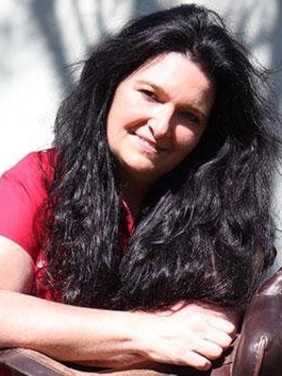 Frau mit langem schwarzem Haar, sitzend, im Sonnenlicht.