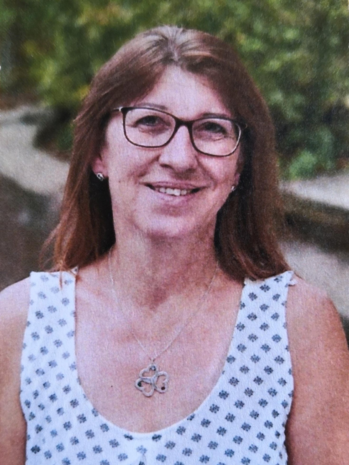 Lächelnde Frau mit Brille und gemustertem Oberteil im Freien.