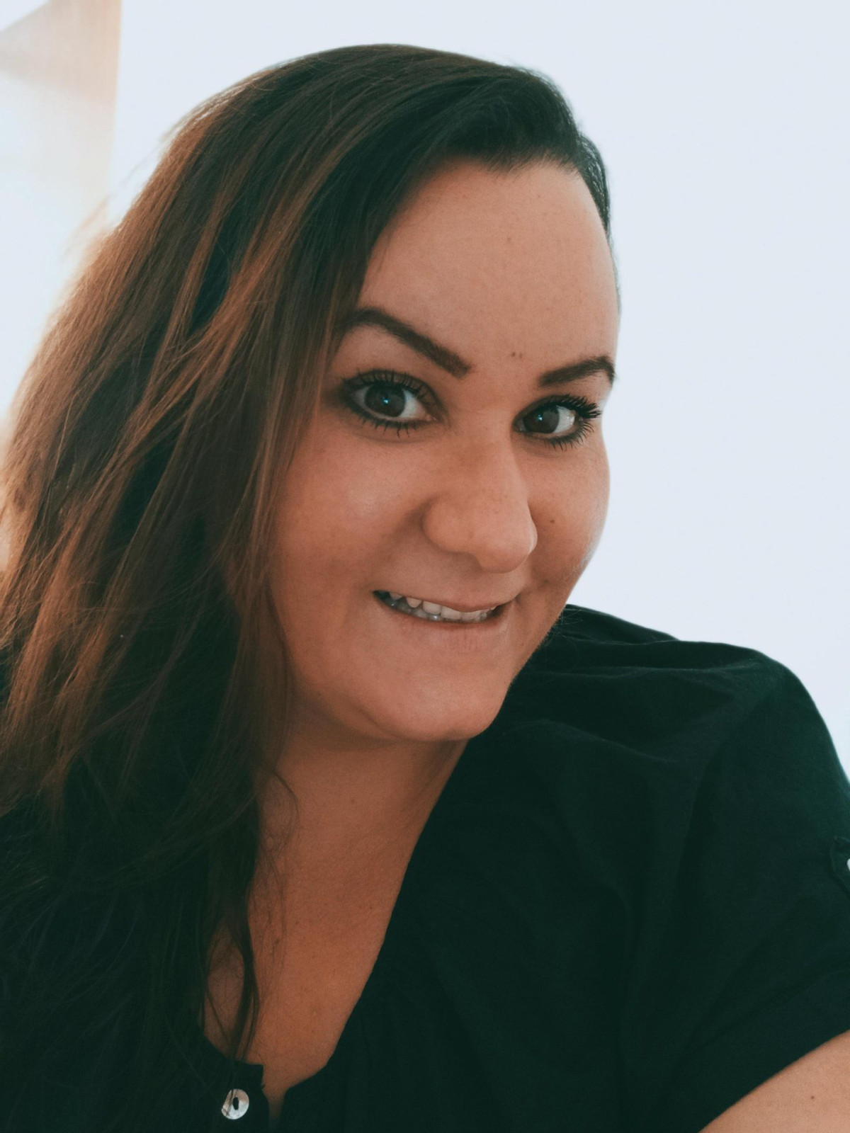 Frau mit langen braunen Haaren, die in die Kamera lächelt, in einem schwarzen Oberteil.