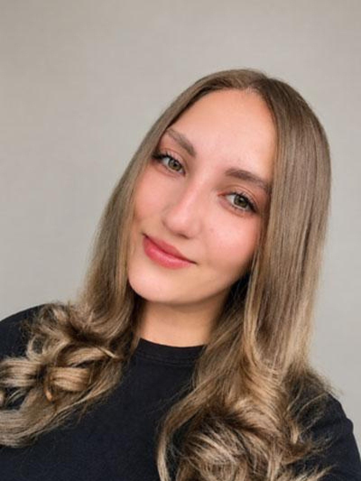 Eine Frau mit langen, gewellten Haaren lächelt sanft in die Kamera.