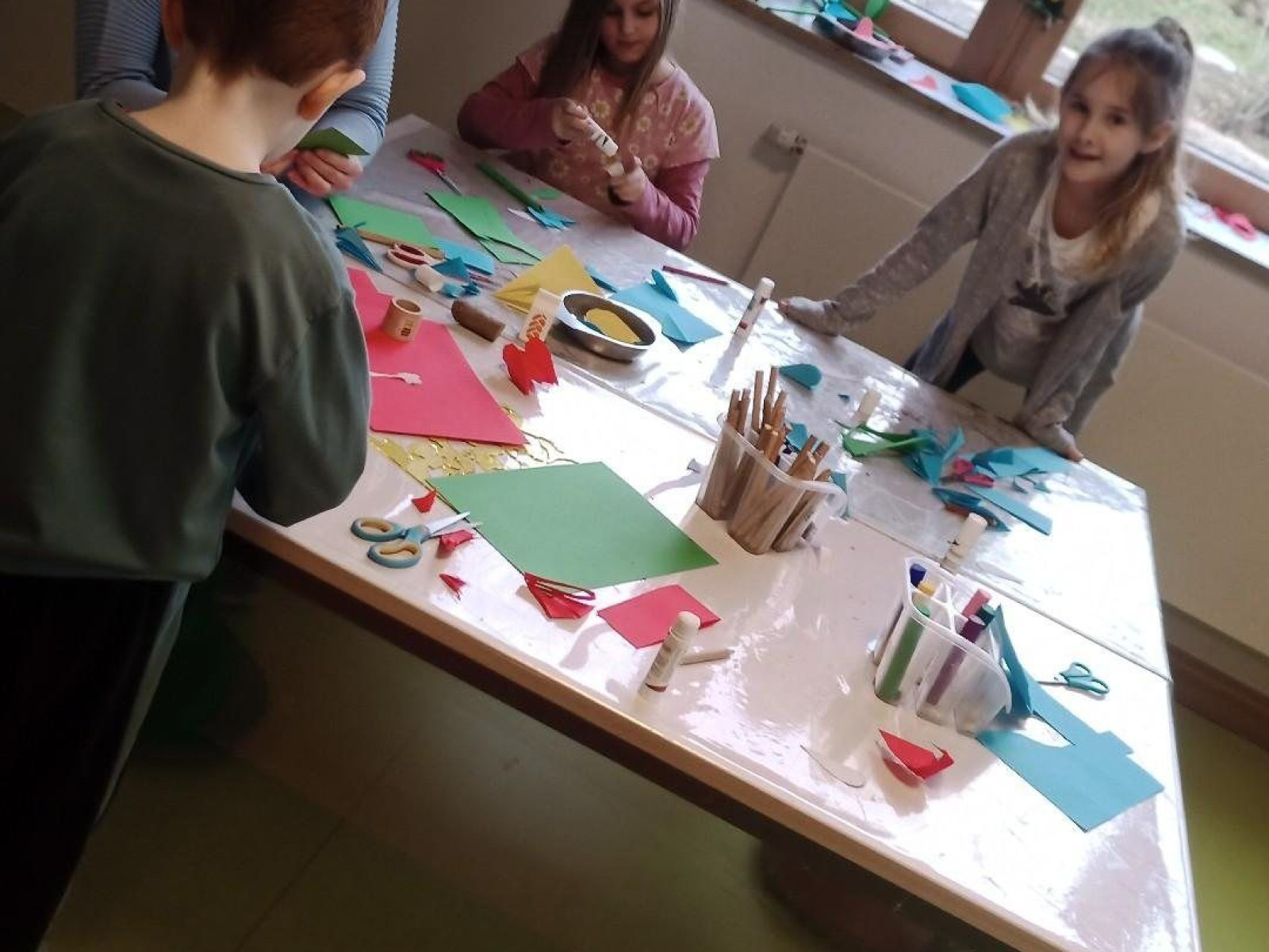 Kinder beim Basteln mit Papier und Scheren an einem Tisch im Raum.