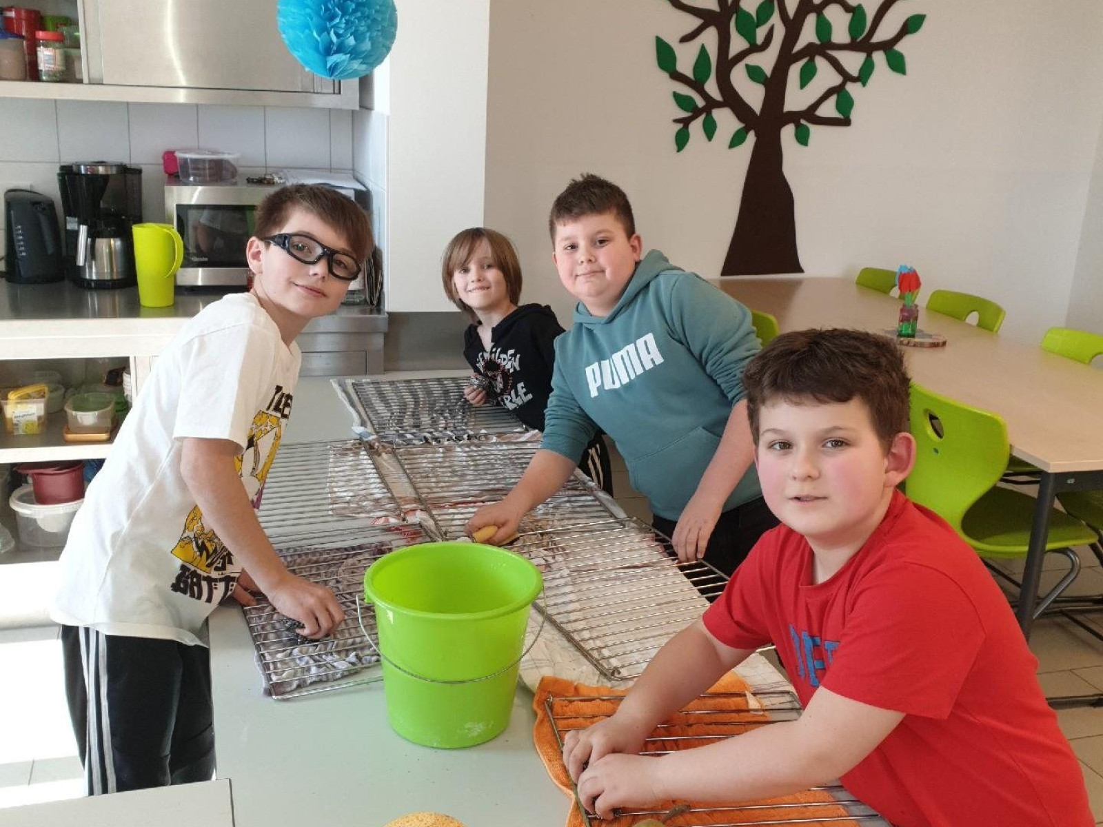Vier Kinder in einer Schulküche schneiden Gemüse an einem Tisch mit Obstkorb.