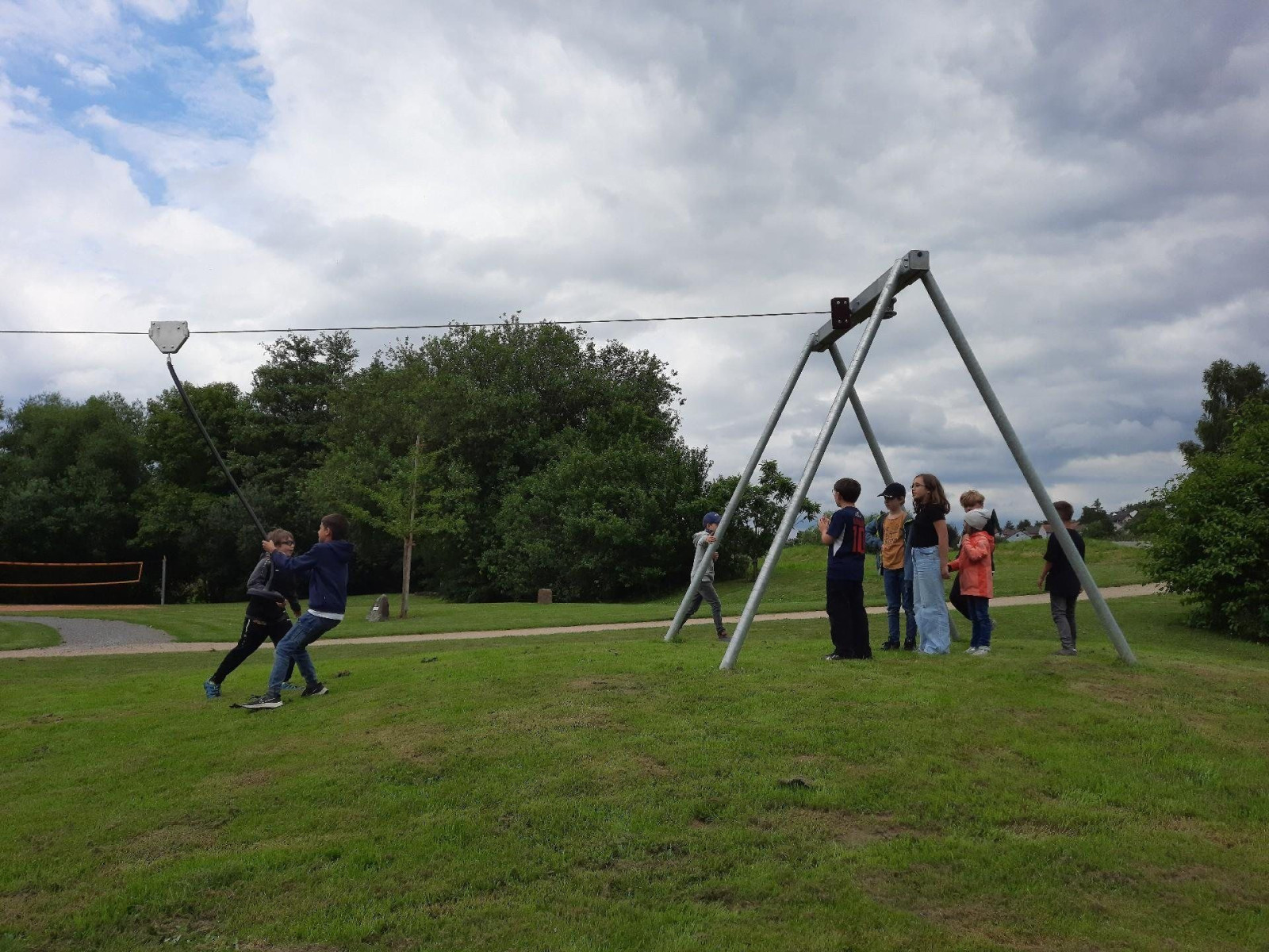 Gruppe von Kindern auf einer Seilrutsche im Park mit bewölktem Himmel.