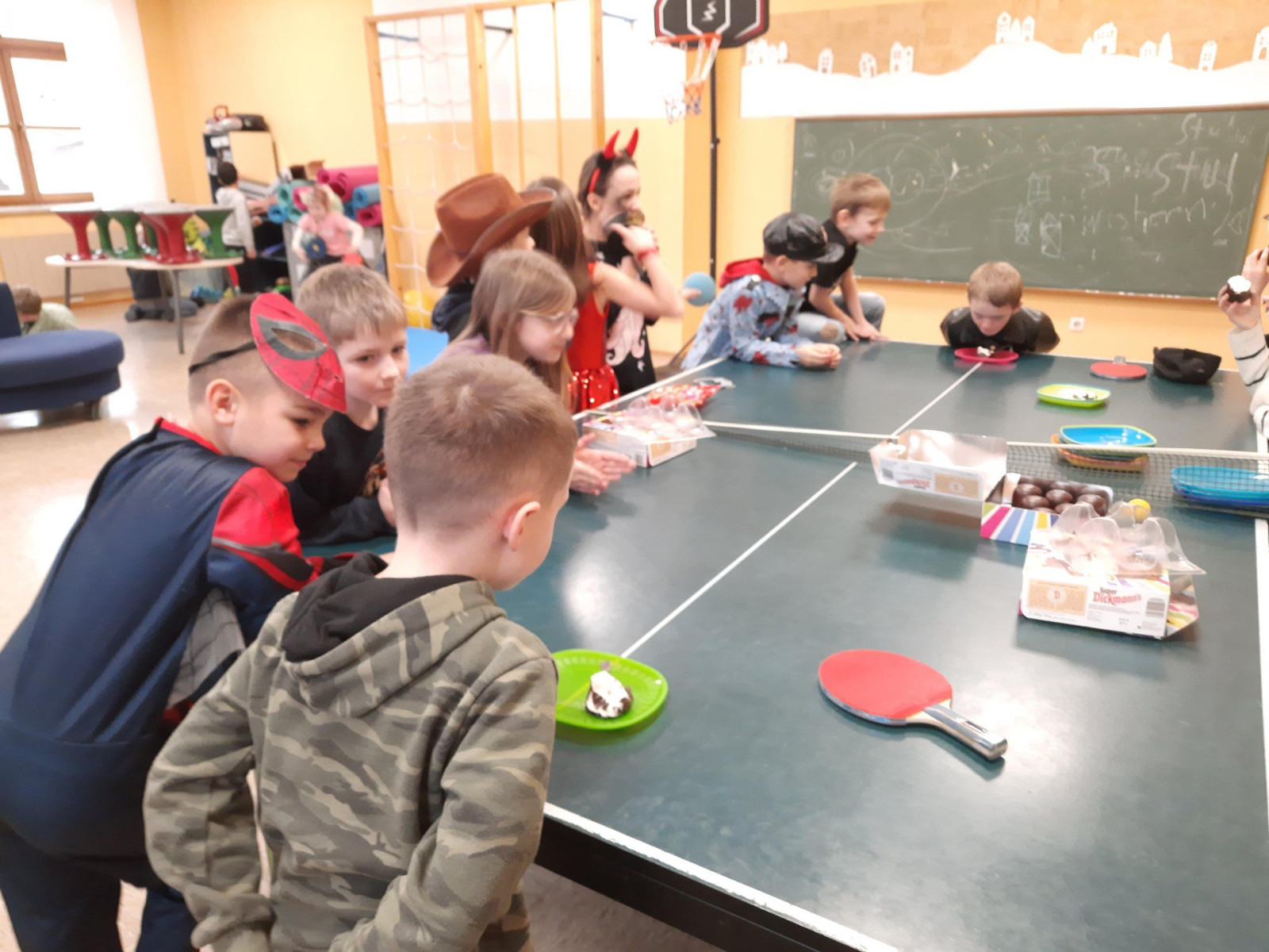 Kinder in Kostümen stehen um einen Tischtennistisch, auf dem Süßigkeiten liegen.