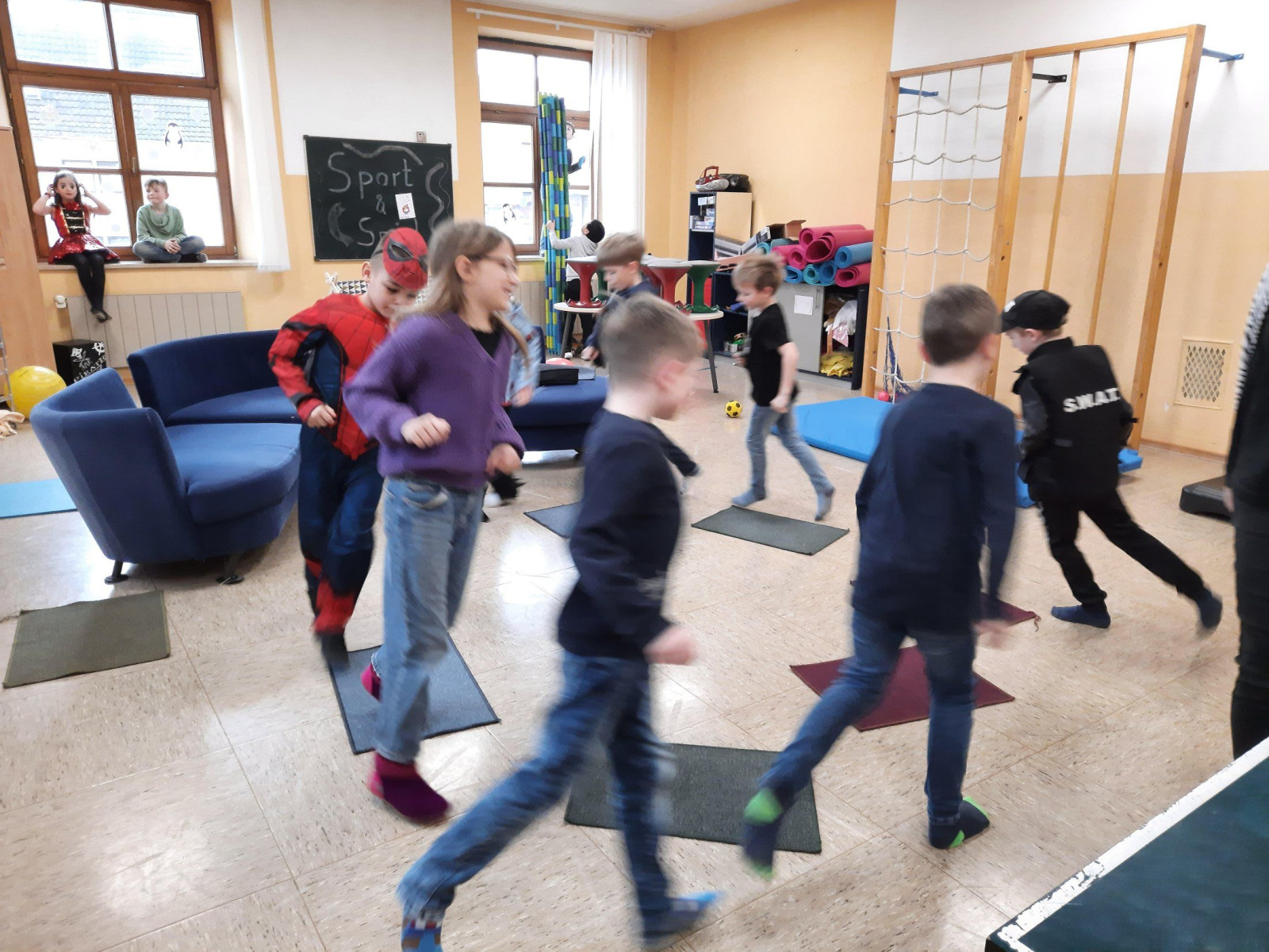 Eine Gruppe von Kindern spielt und rennt in einem Raum mit Klettergeräten und Matten.