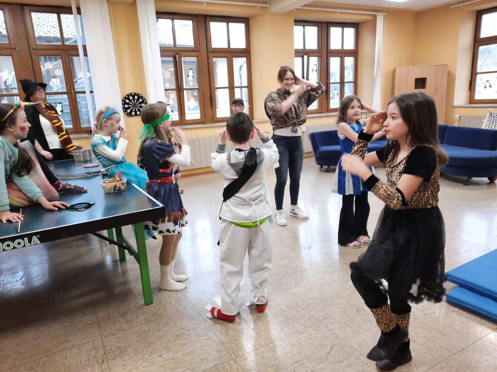 Kinder in verschiedenen Kostümen spielen fröhlich in einem Raum mit einer Tischtennisplatte.