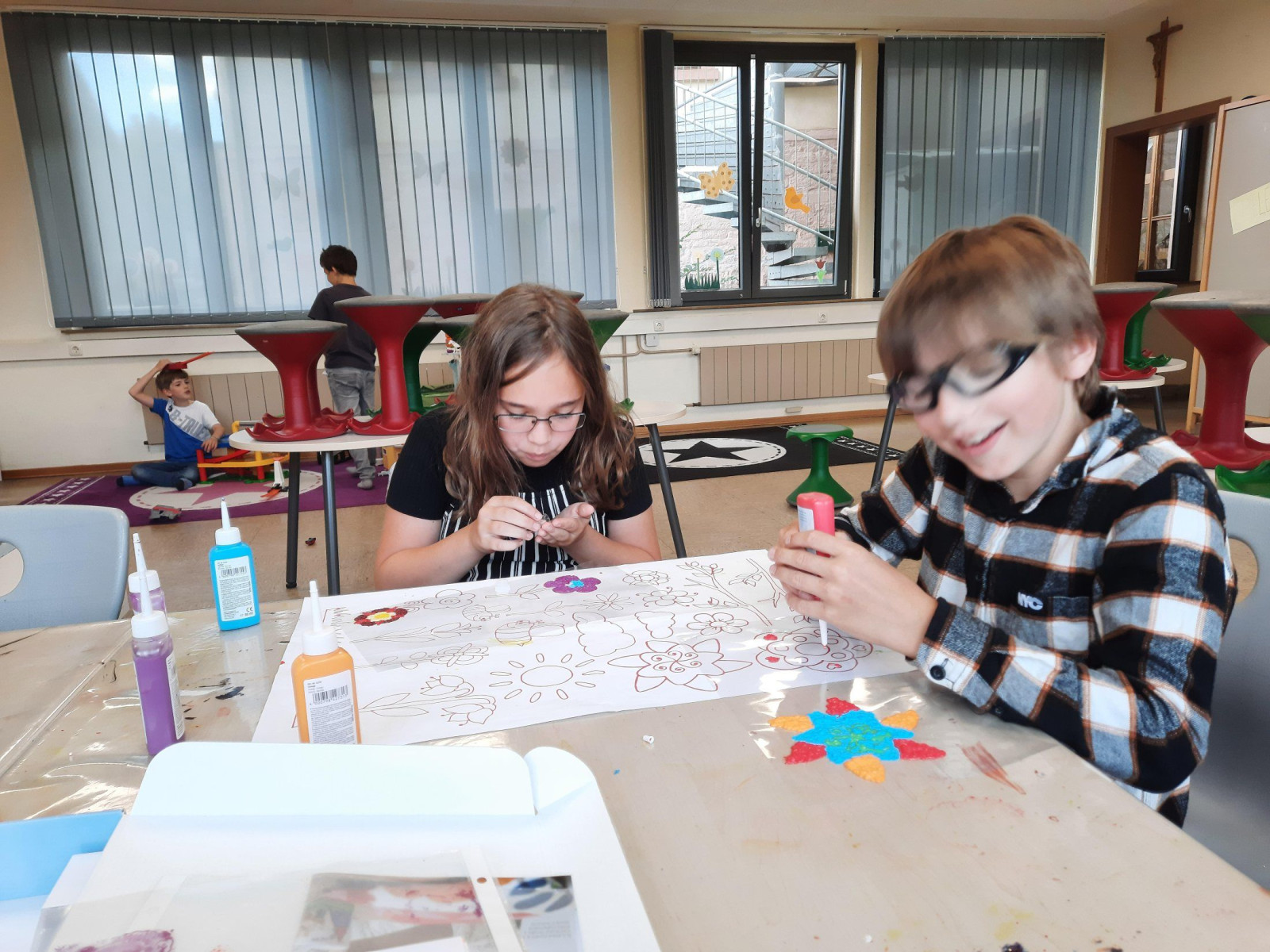 Zwei Kinder arbeiten an einem Kunstprojekt mit Papier und Farben in einem Klassenzimmer.