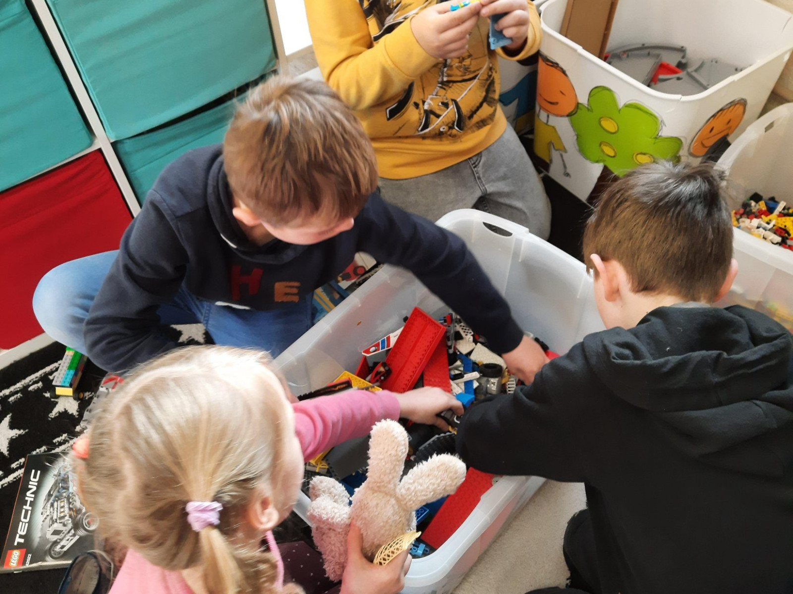 Gruppe von vier Kindern, die im Spielzimmer Lego bauen, neben bunten Aufbewahrungsboxen.