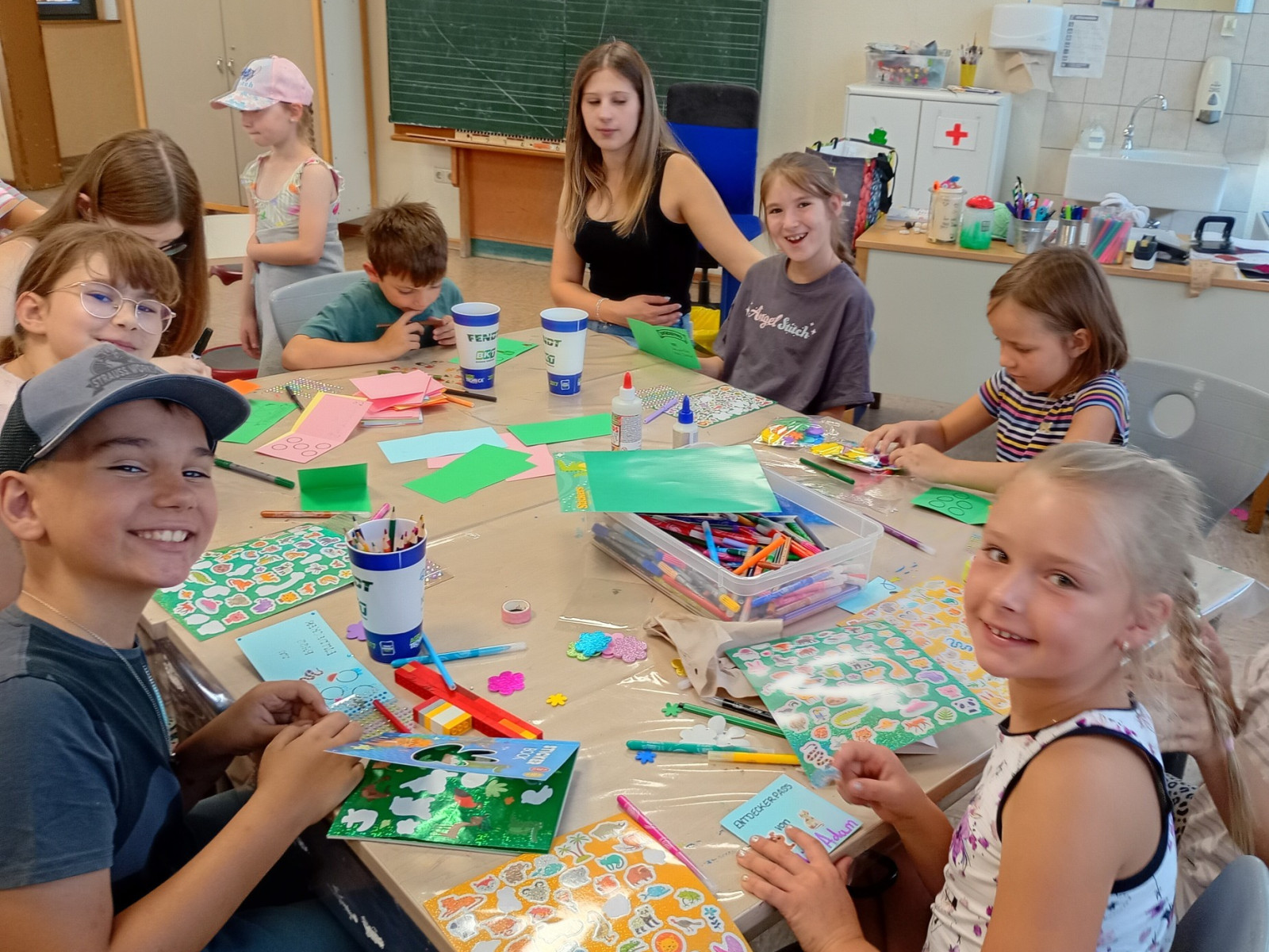 Gruppe von Kindern beim Basteln an einem Tisch mit Papier und Aufklebern.