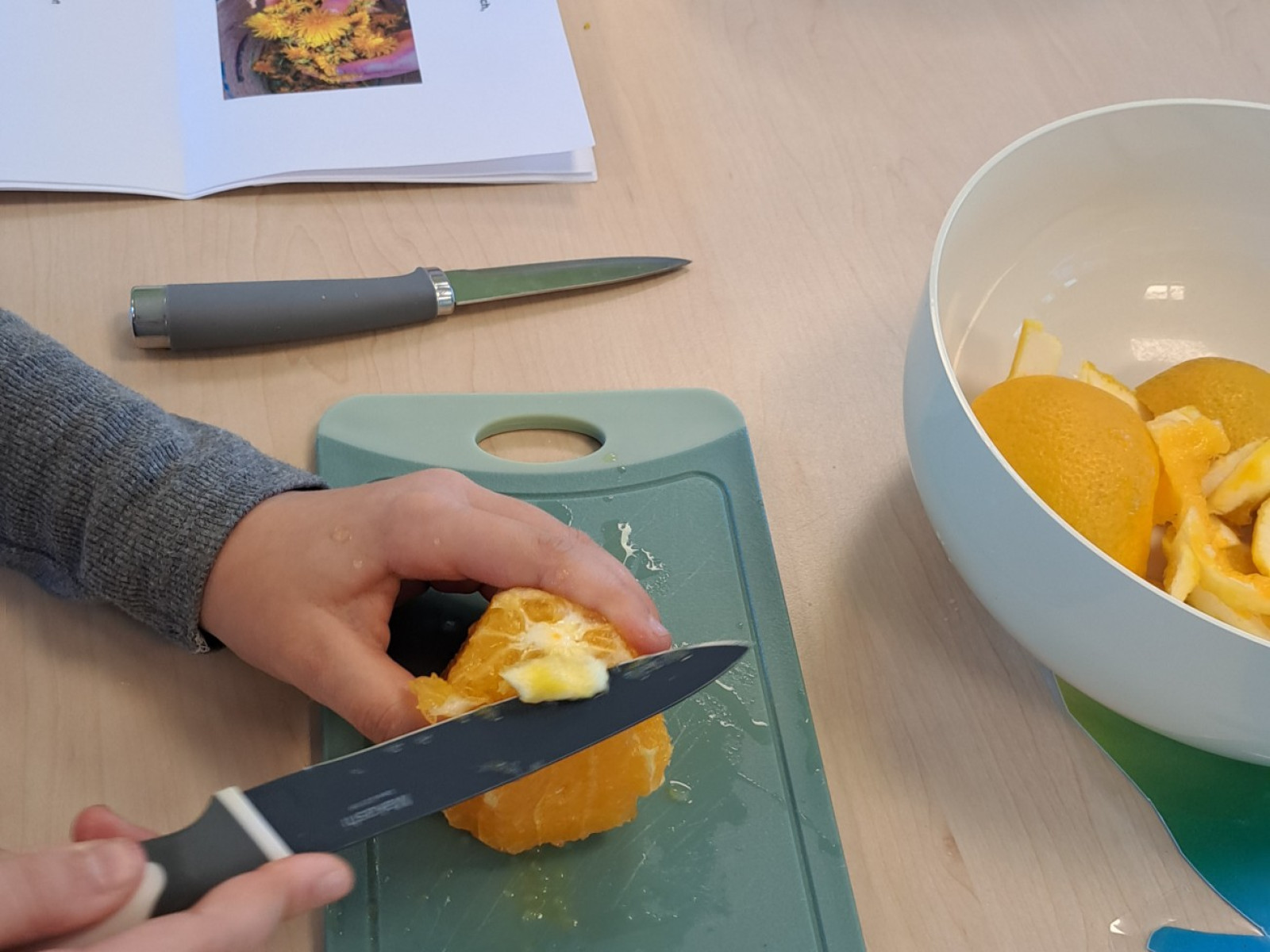 Kind schält eine Orange mit einem Messer auf einem Schneidebrett in der Küche.