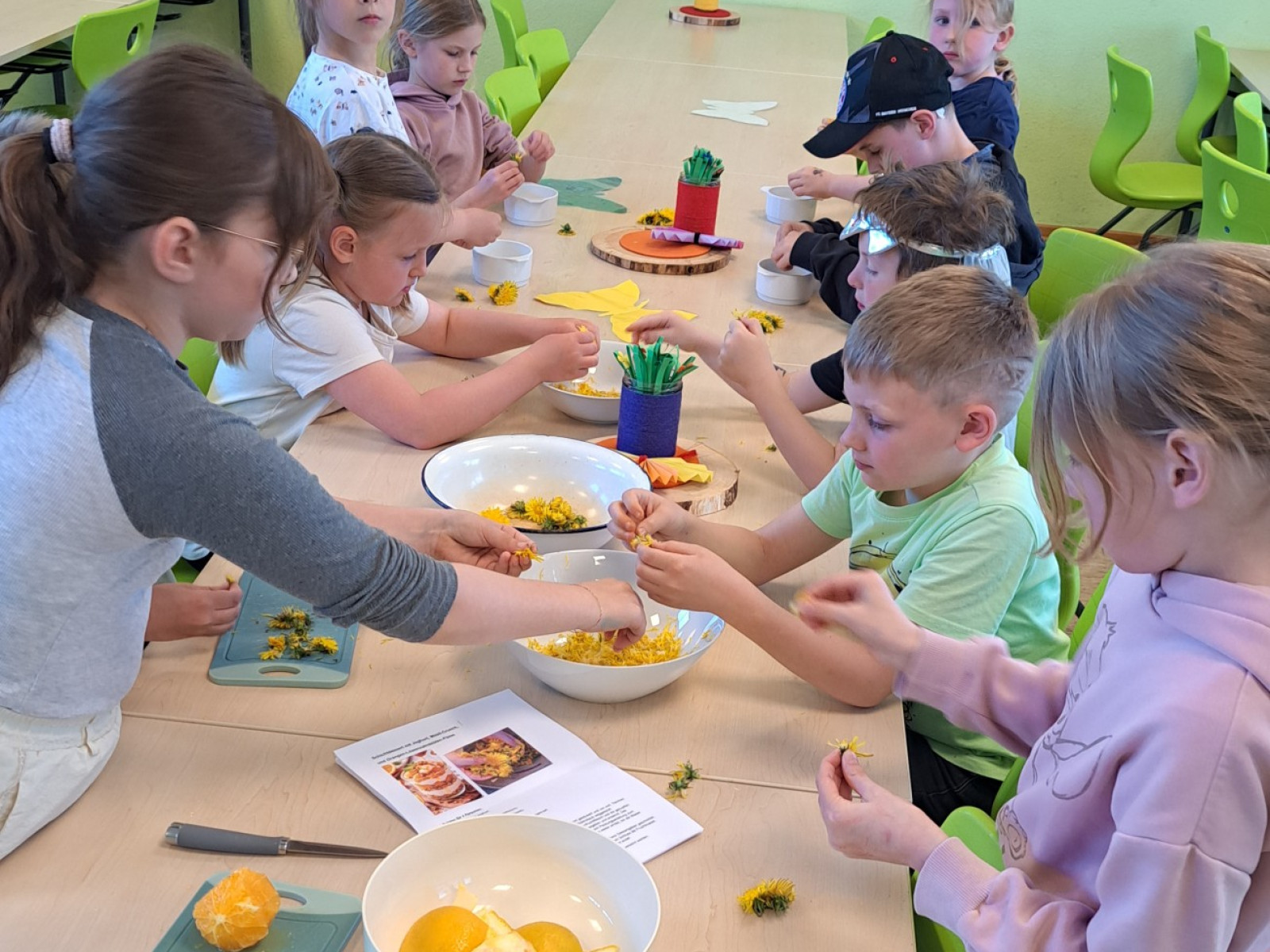 Kinder sitzen an einem Tisch und schneiden Obst zur gemeinsamen Zubereitung von Speisen.