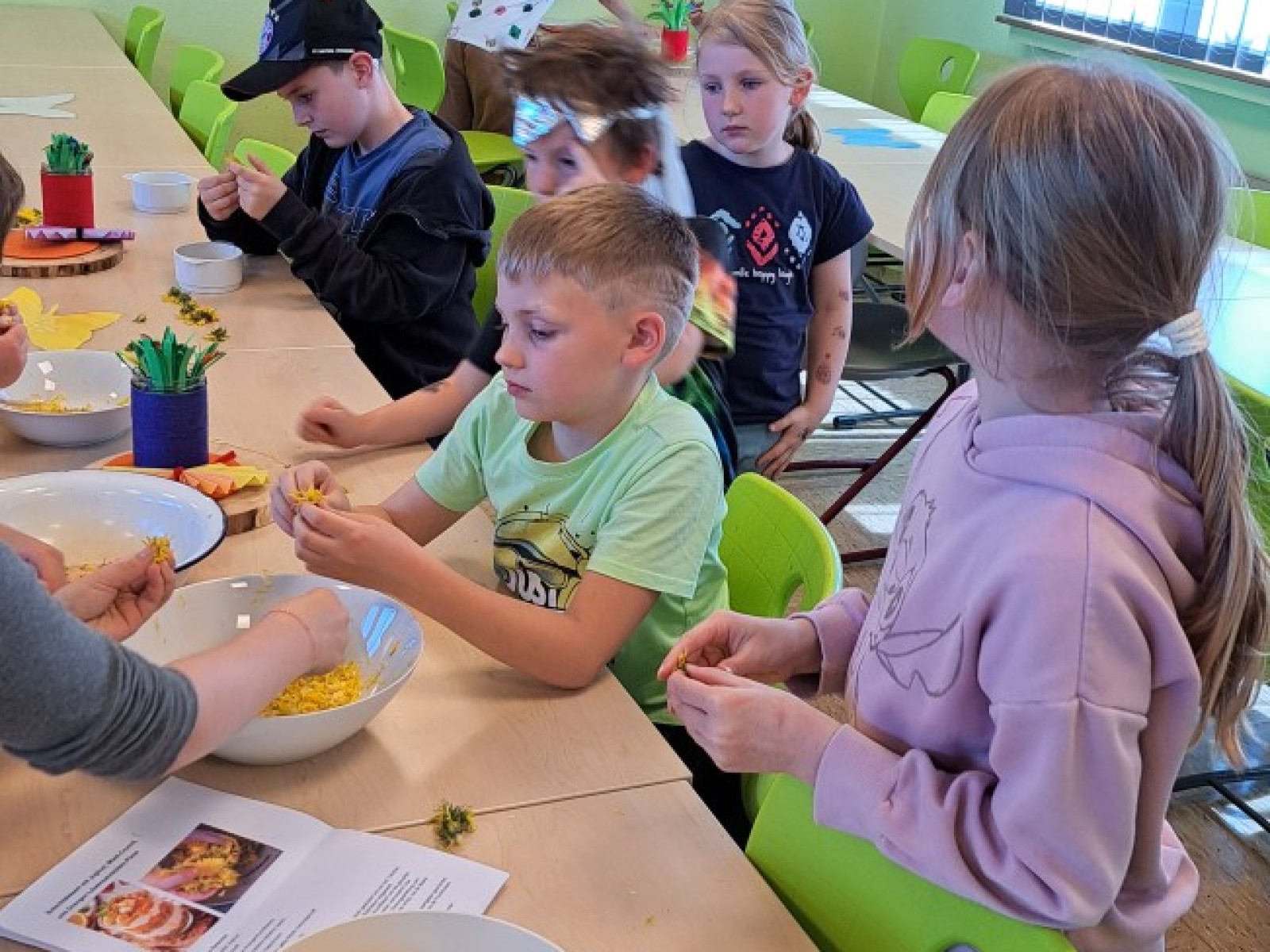 Kinder in einer Schulküche schälen Zitronen an einem Tisch, umgeben von bunten Dekorationen.