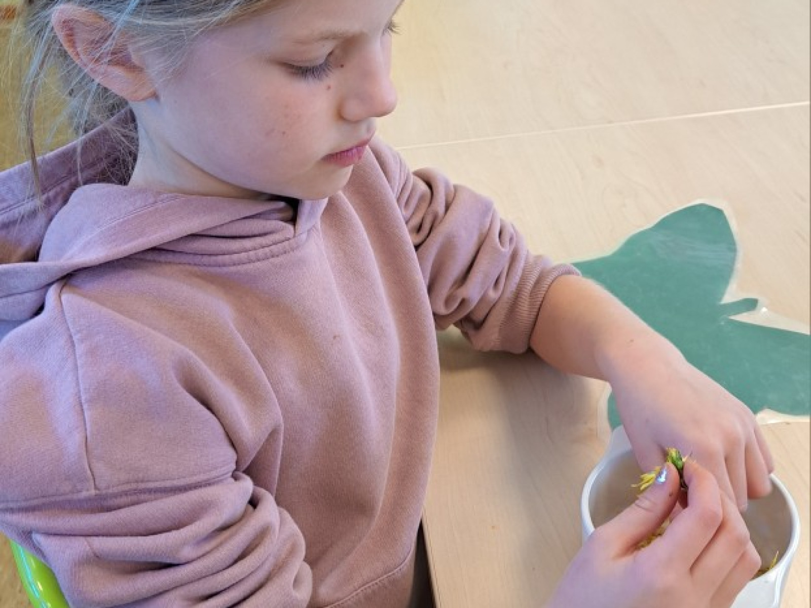 Kind in rosa Pullover schneidet an einem Tisch mit Schere und Papierauschnitt.