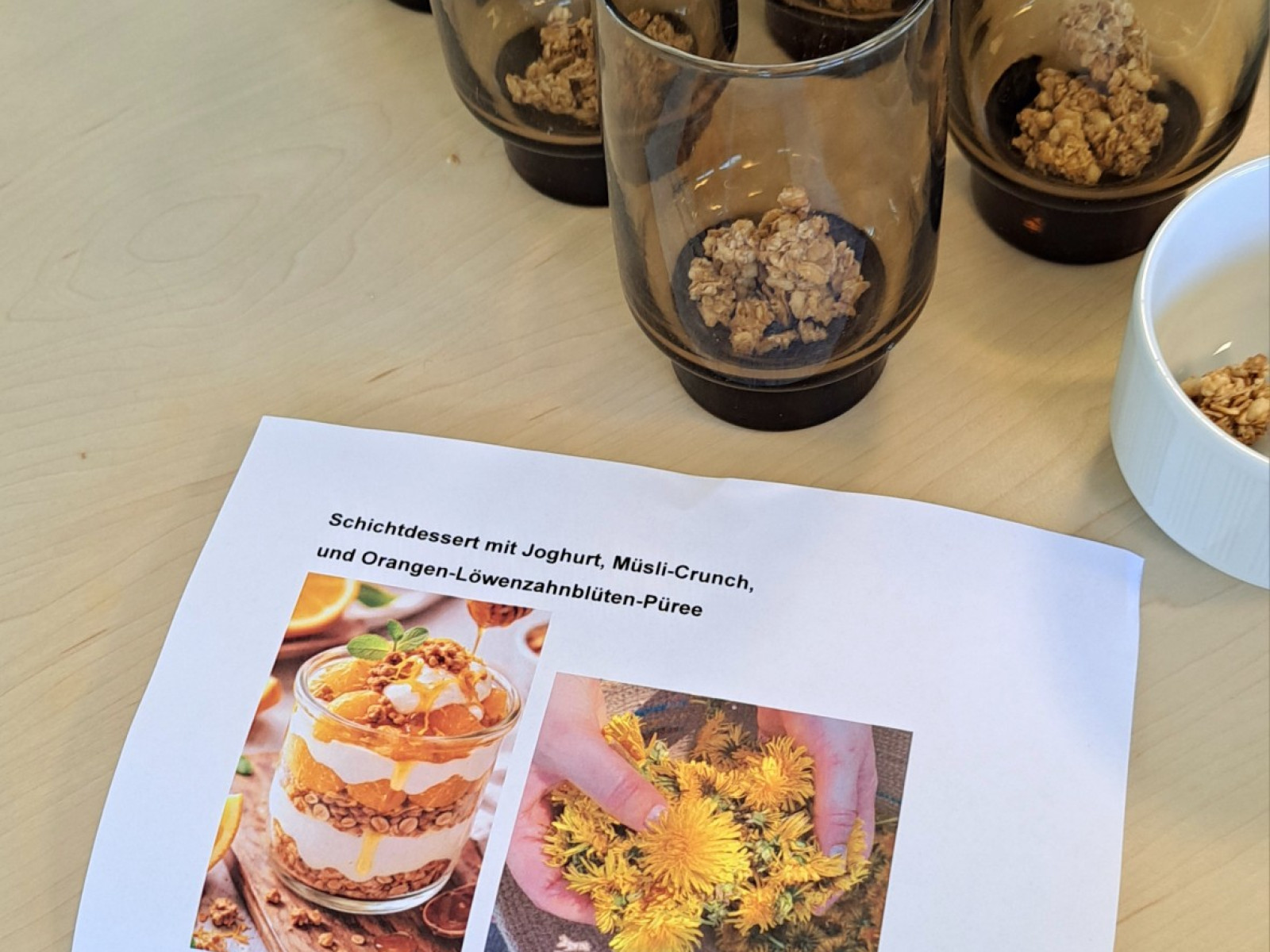 Mehrere Gläser mit Schichtdessert und ein Rezeptblatt auf einem Tisch.