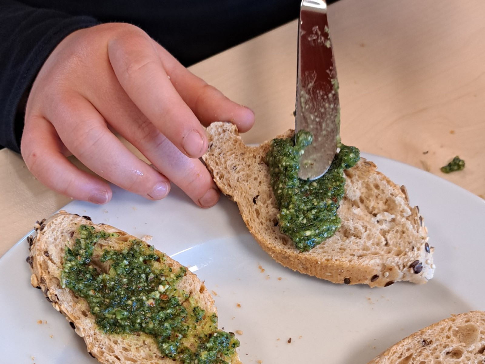 Hände verteilen grünes Pesto auf Brotscheiben auf einem Teller.