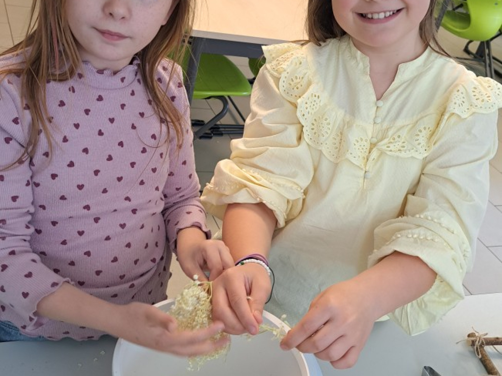 Zwei Mädchen in einer Schulküche, die eine Mahlzeit zubereiten. Auf einem Tisch sind Zutaten verteilt.