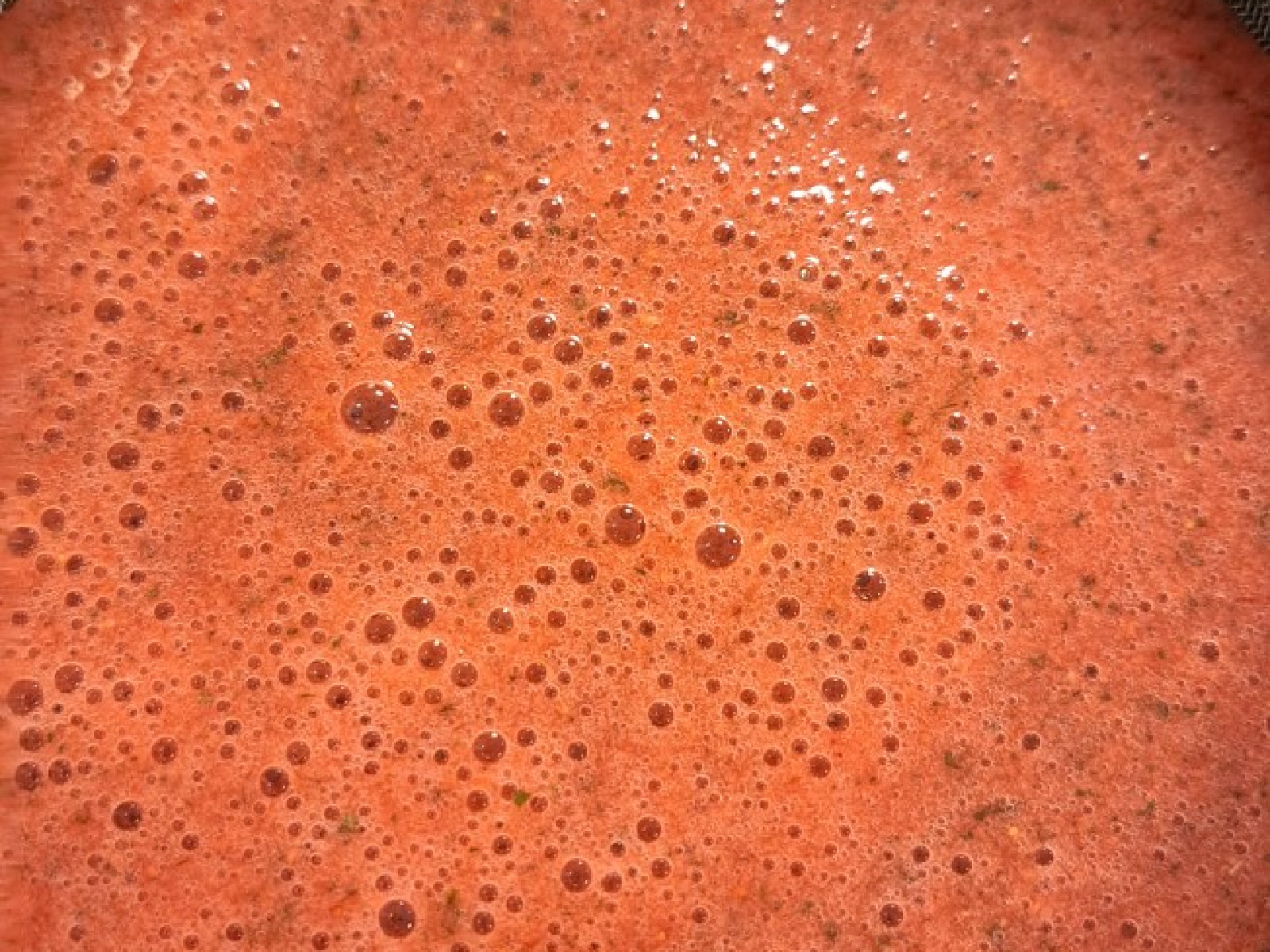 Roter Beeren-Smoothie, der durch ein Sieb in einer Metallschüssel gefiltert wird.