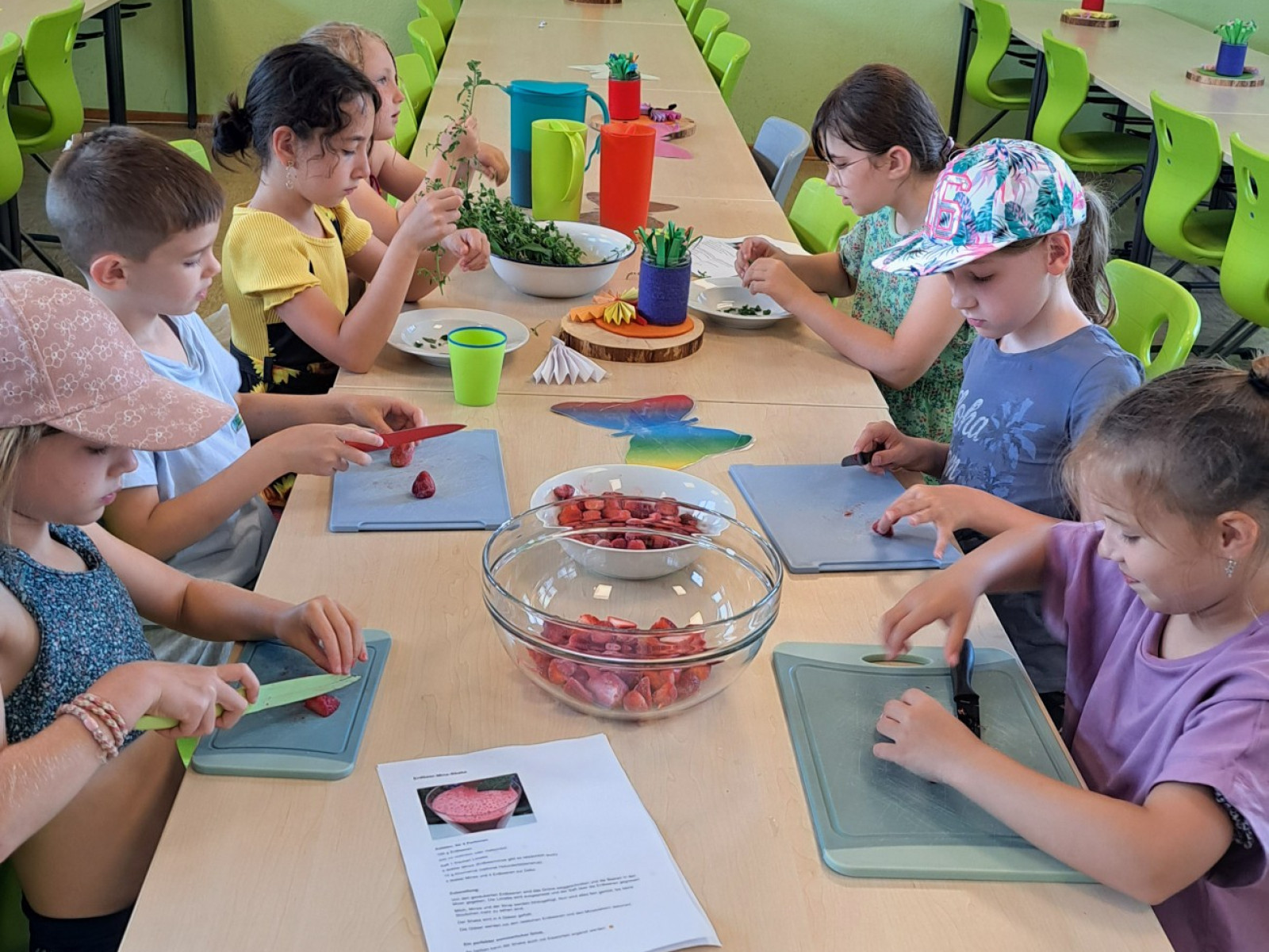 Kinder am Tisch schneiden Obst bei einem Kochkurs, mit Schneidebrettern und Schalen voller Obst.