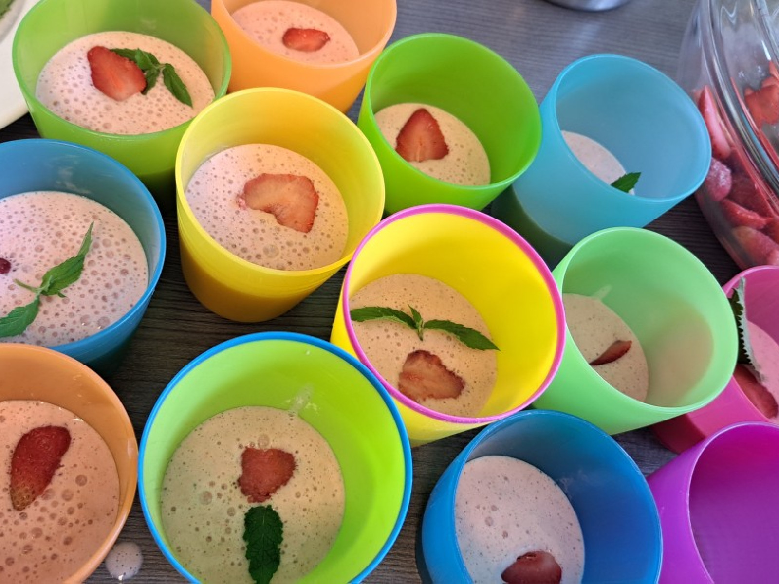 Bunte Plastikbecher mit schaumigem Dessert, verziert mit Erdbeer- und Minzblättern.