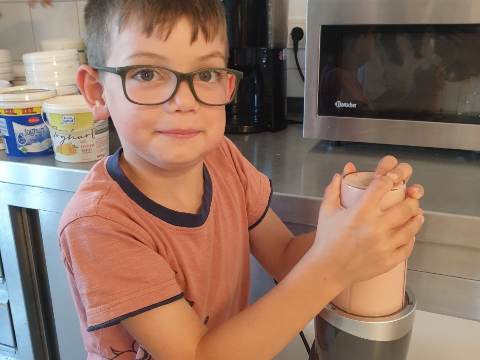 Junge mit Brille bedient Mixer in der Küche, umgeben von Küchengeräten.