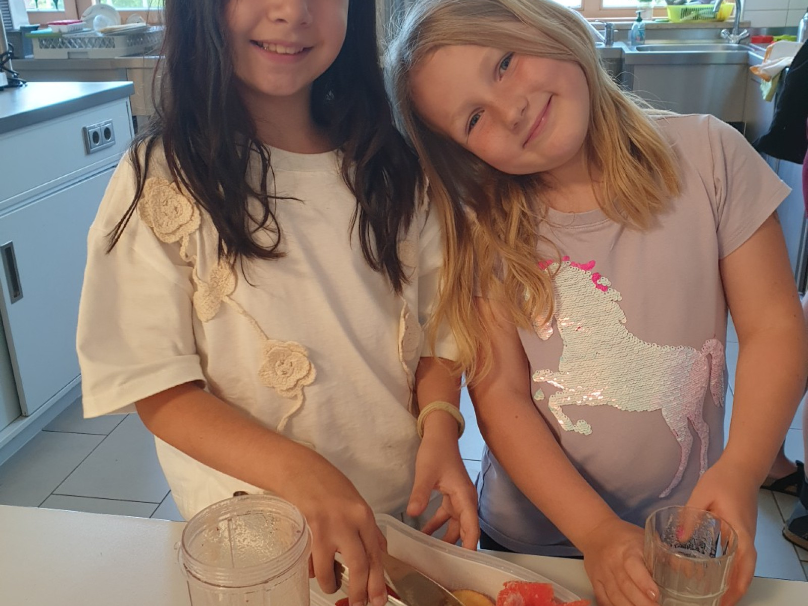 Zwei Mädchen stehen in der Küche, bereiten Obst zu und lächeln dabei.
