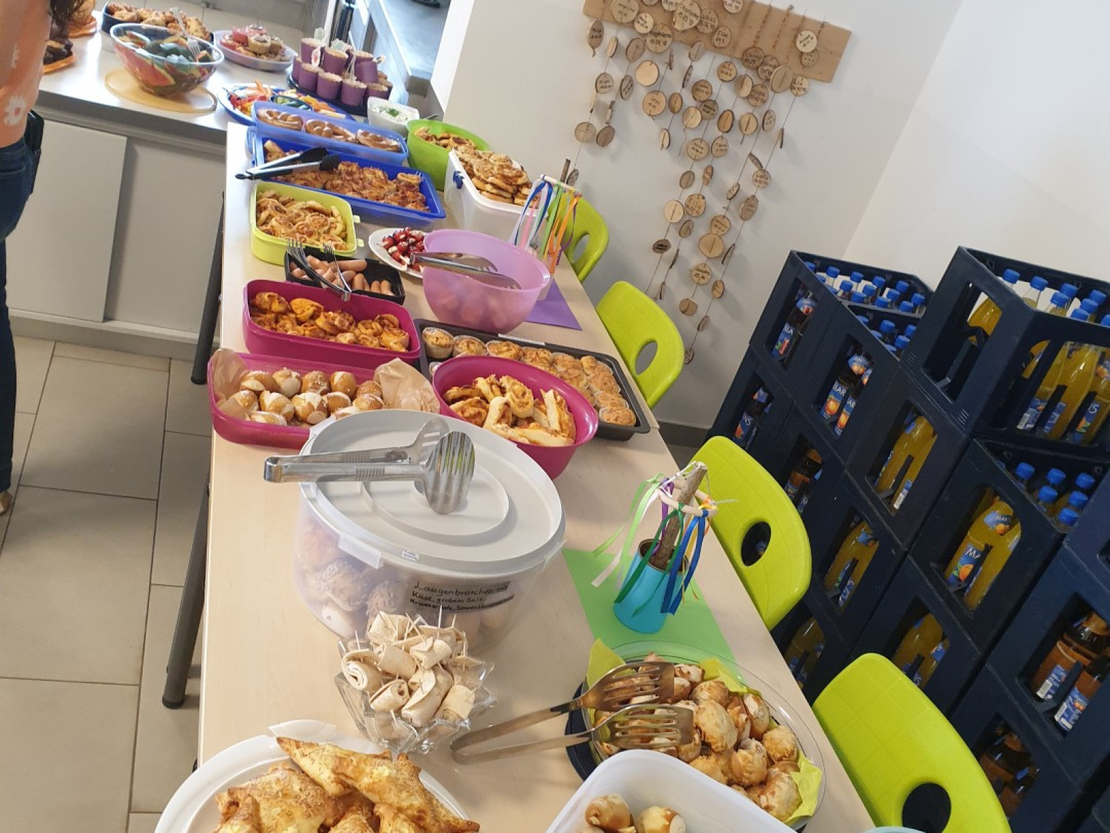 Ein Tisch in einer Küche, bedeckt mit verschiedenen Tellern voller Snacks und Gebäck, daneben Getränkekästen gestapelt.