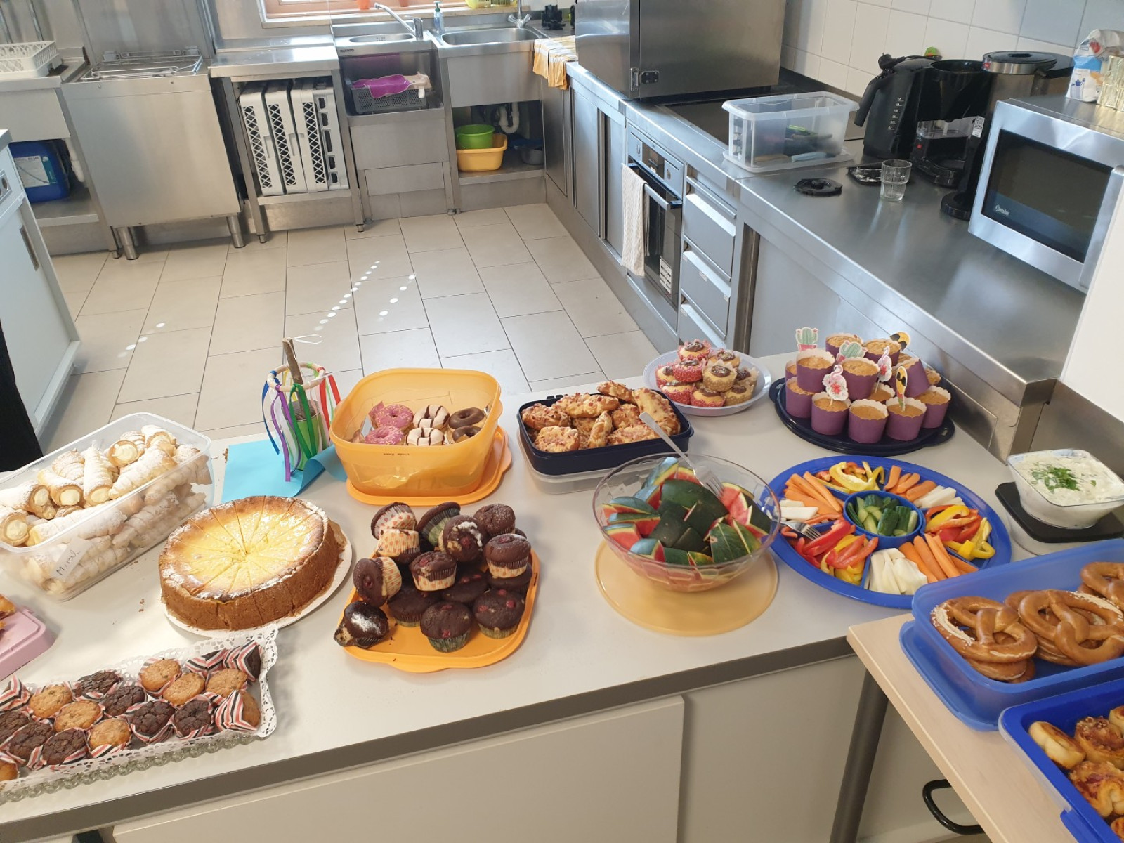 Buffet mit Kuchen, Gebäck, Muffins, und mehr in einer modernen Küche mit Edelstahlgeräten.