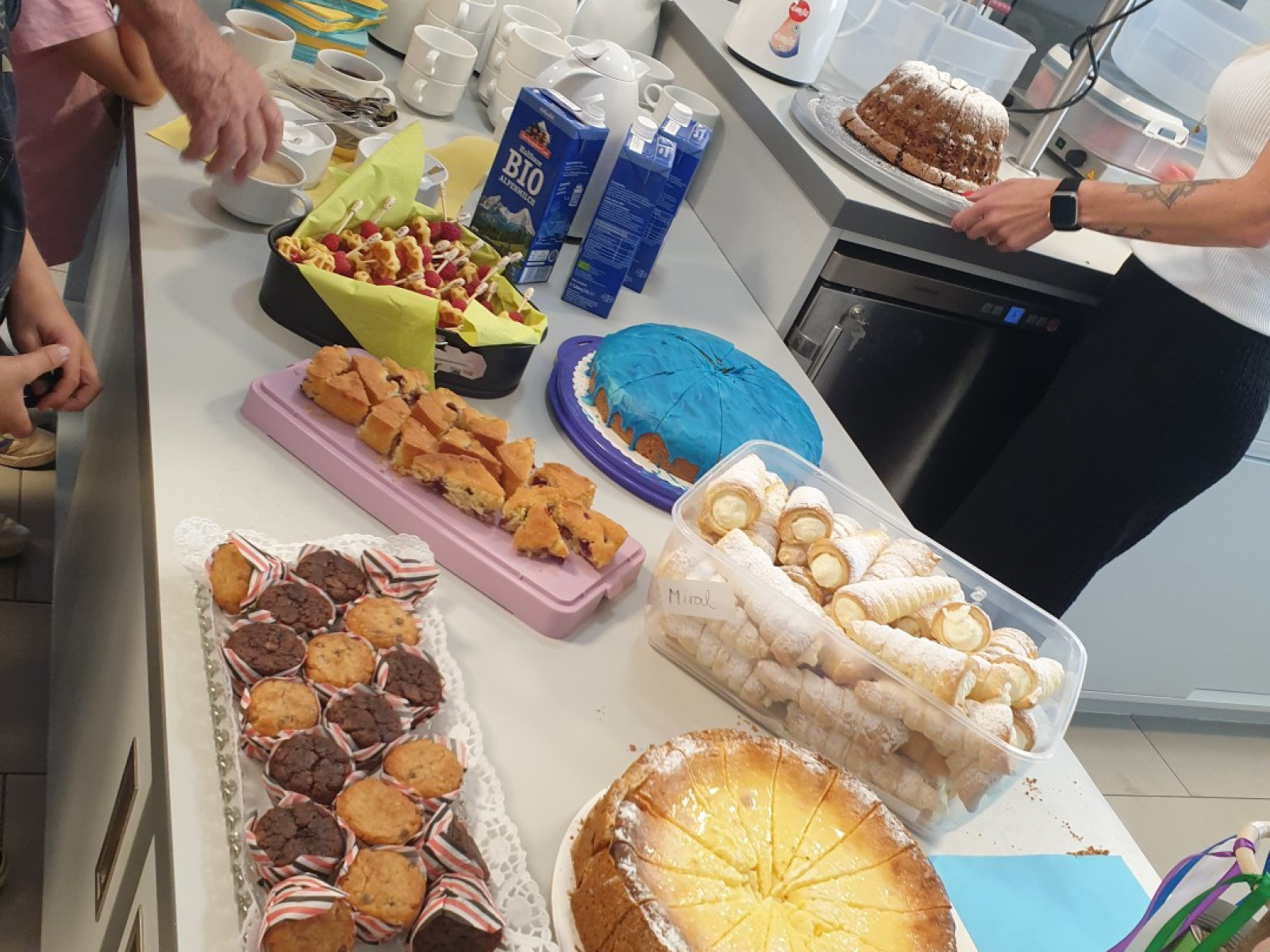Ein Tisch voller verschiedener Kuchen, Kekse, Snacks und Getränke in einer geselligen Umgebung.